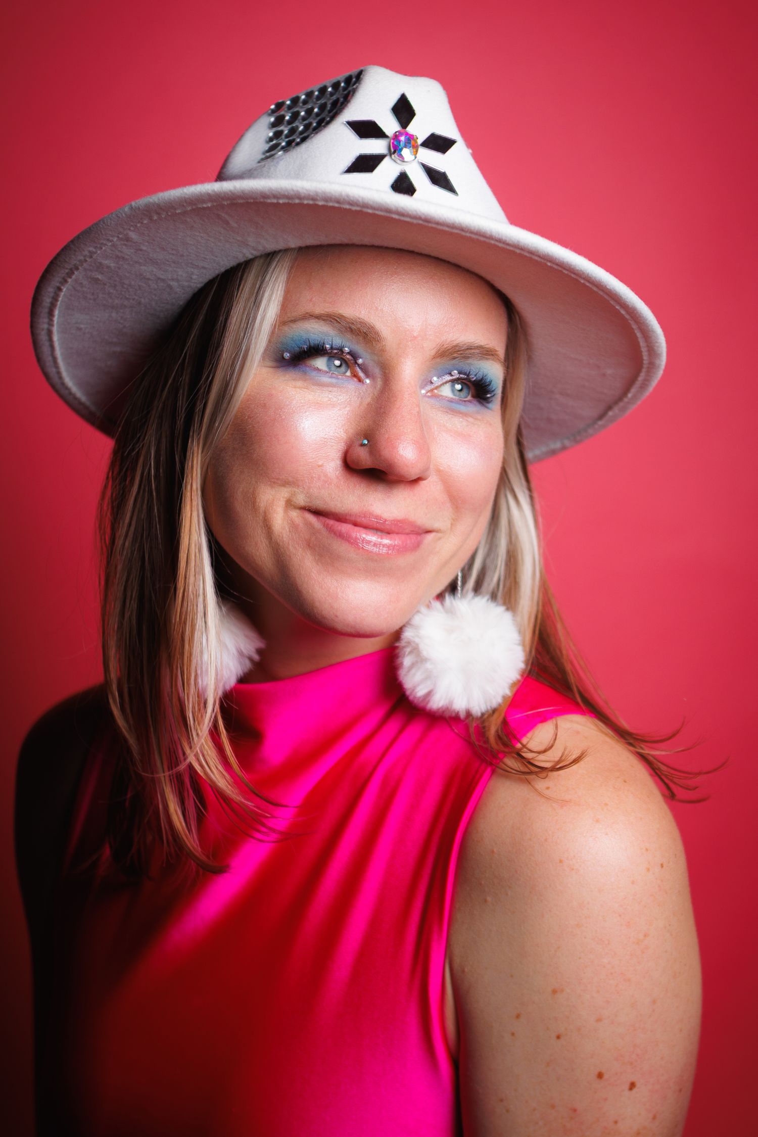 Woman in a pink sleeveless top with a white hat, smiling, indoor studio with pink background.