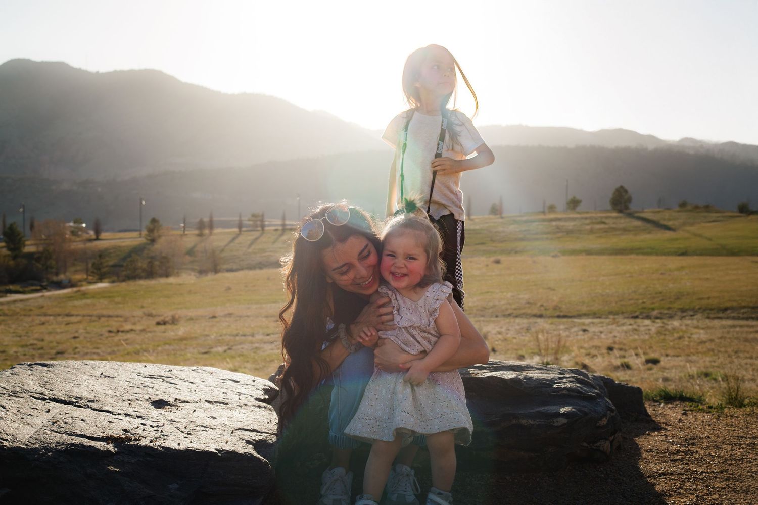Family portrait at golden hour — mother and young daughter on a rock with mountains behind them, Littleton, CO family photography.