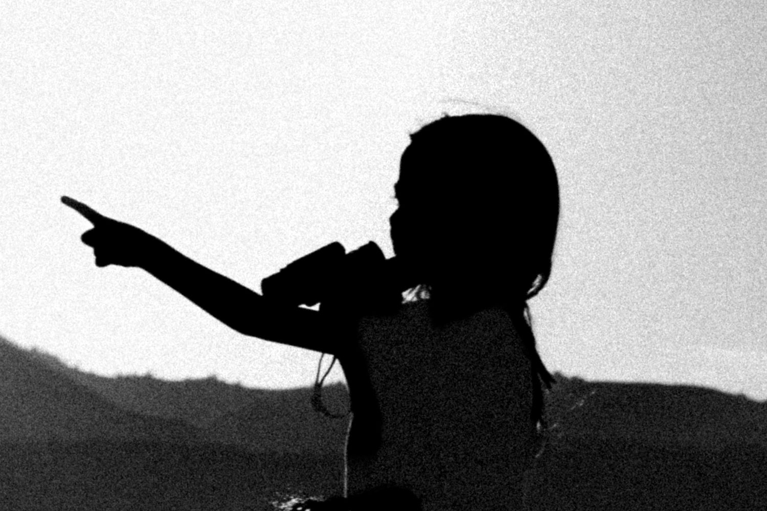 lack-and-white silhouette of a child pointing while standing outdoors.