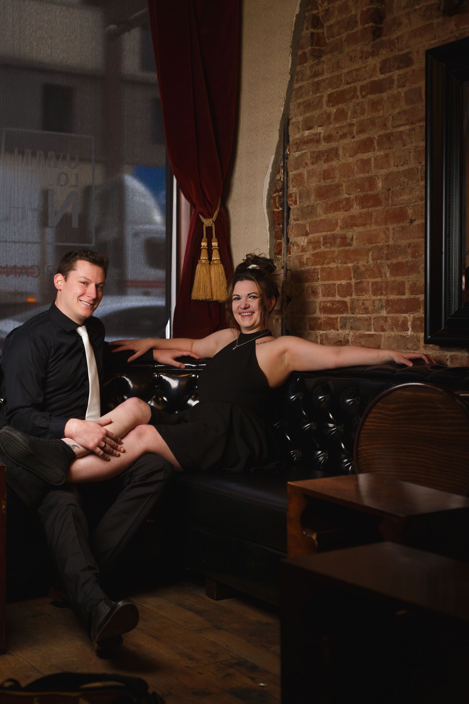 Couples portrait — well-dressed couple in a warmly lit brick-walled lounge, engagement photography in Littleton, CO by Graham Tipton.