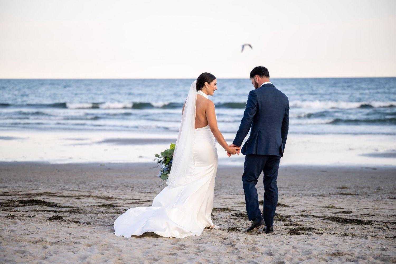 A bride and groom sharing a romantic moment on the sandy shore during their beach wedding in Narragansett, Rhode Island.