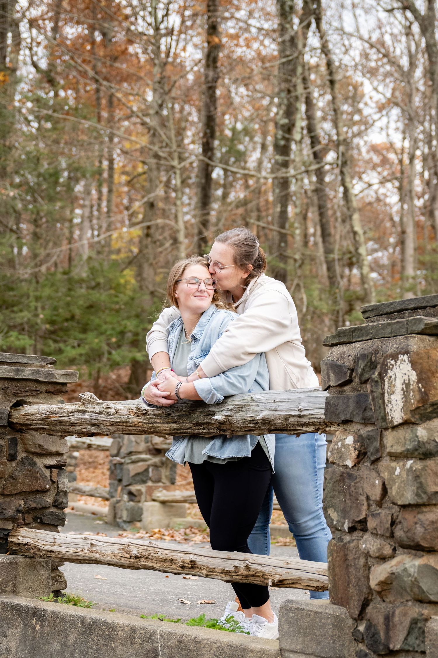 A couple shares an intimate moment on rustic stone steps surrounded by autumn trees in a forest setting.