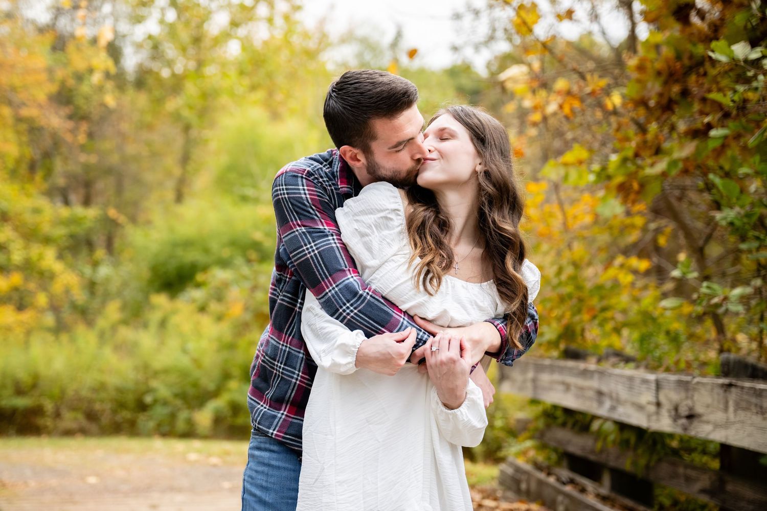 Couple laughing and enjoying a playful moment together while walking through an autumn forest with fallen leaves.