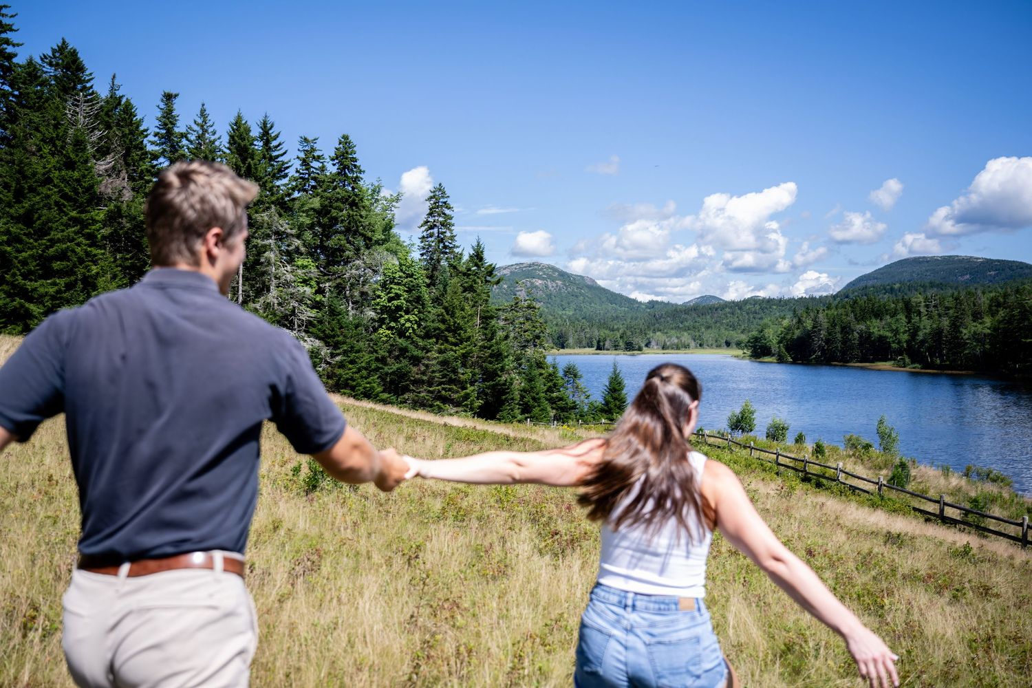 Panoramic mountain views frame a pair of outstretched arms against a tranquil lake and evergreen forest landscape.