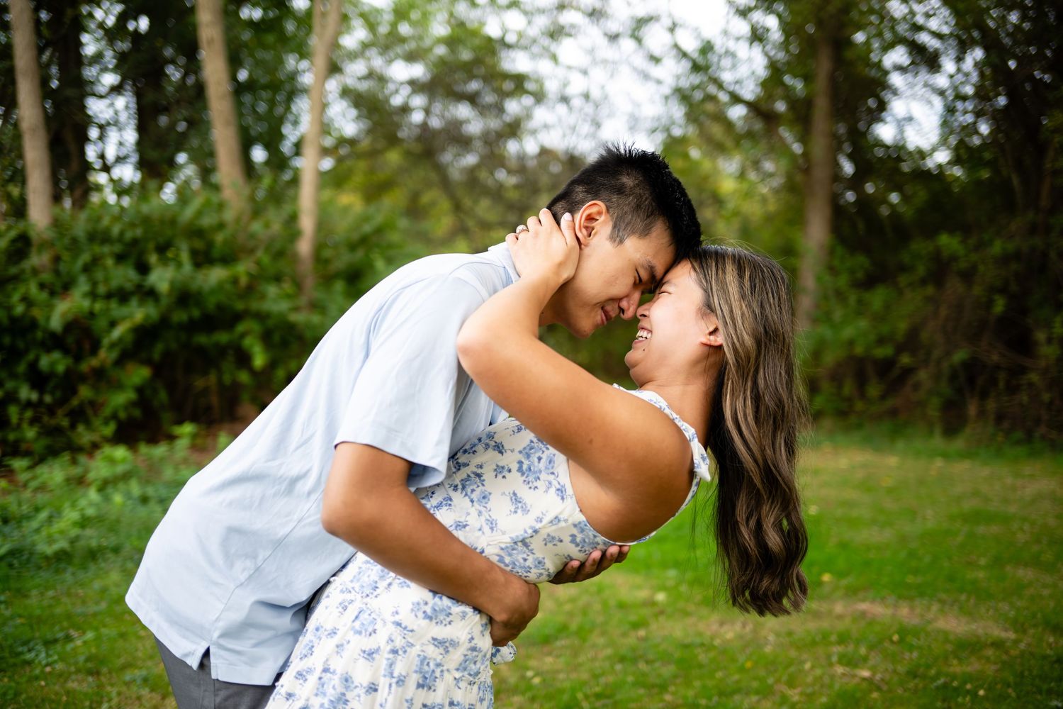 A couple in white outfits share romantic kisses during a photo session in a lush green outdoor setting.