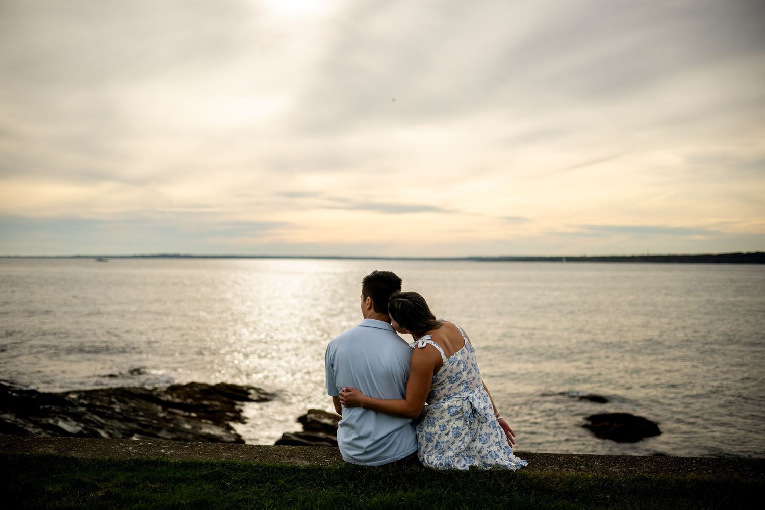 An engaged couple embracing at sunset along the rocky coastline of Brenton Point State Park in Newport, Rhode Island.