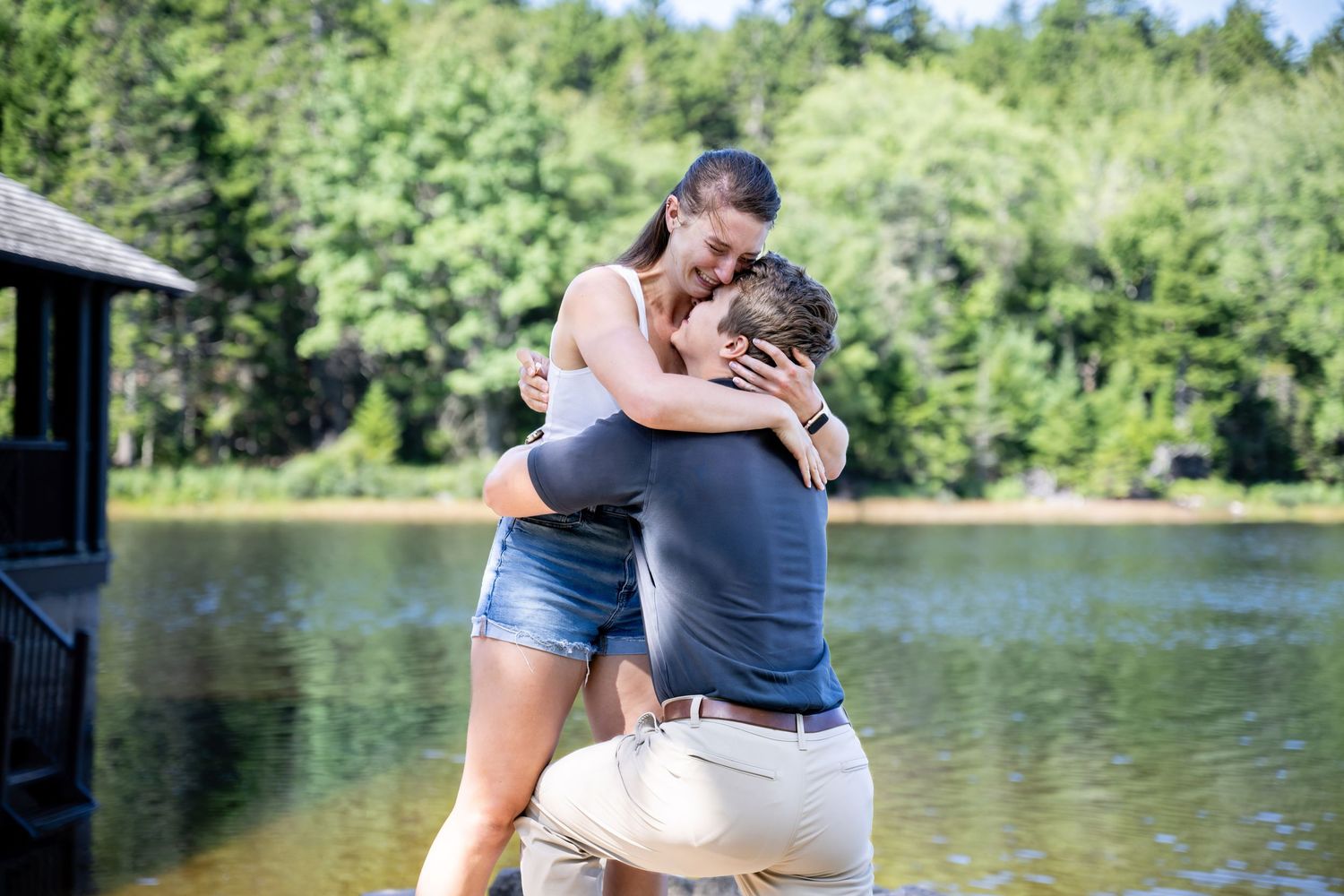 A couple embraces while standing by a scenic lakeside trail on a sunny summer afternoon.