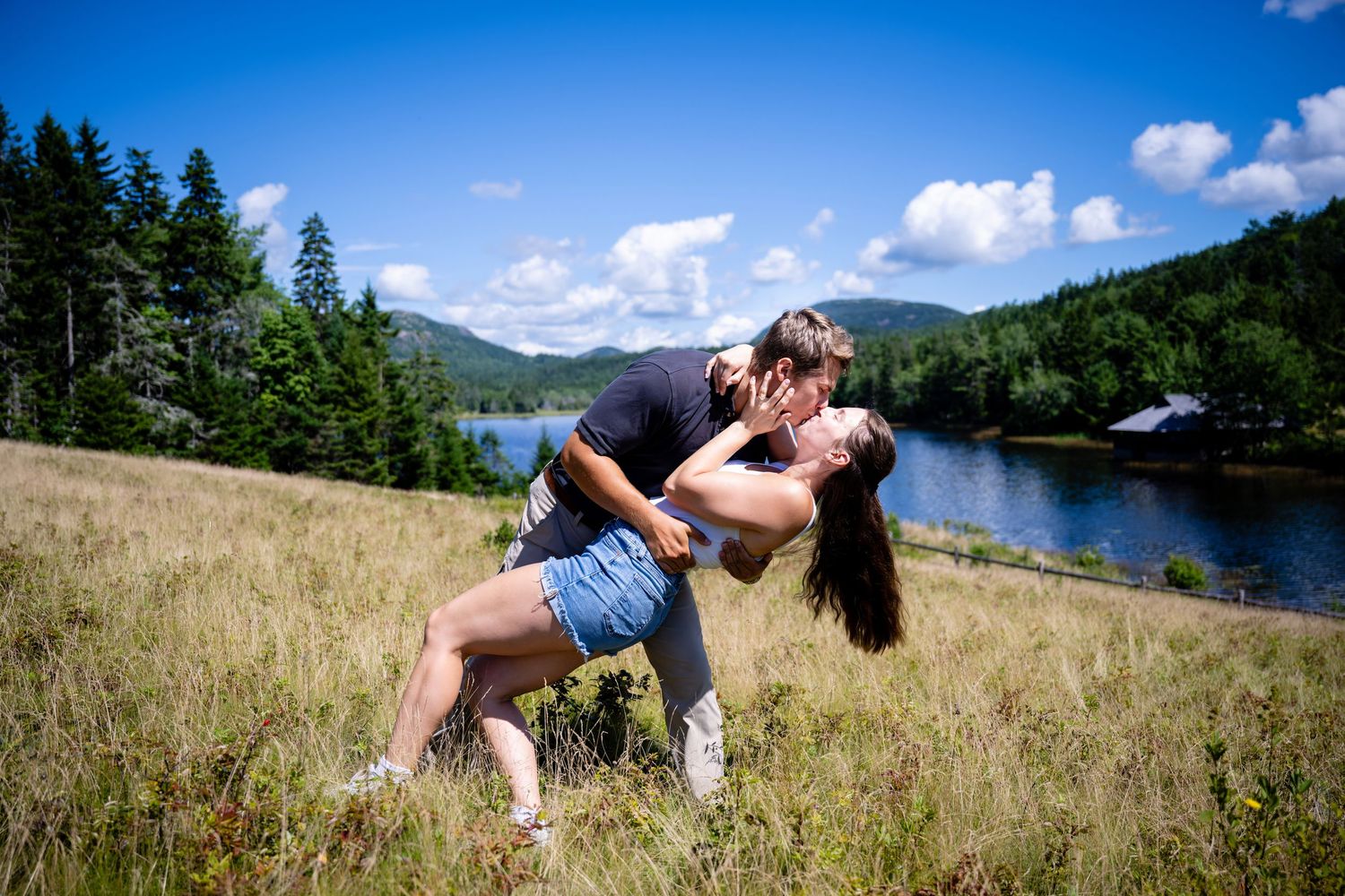Panoramic sequence of affectionate couple embracing in field with lake and mountains in background.