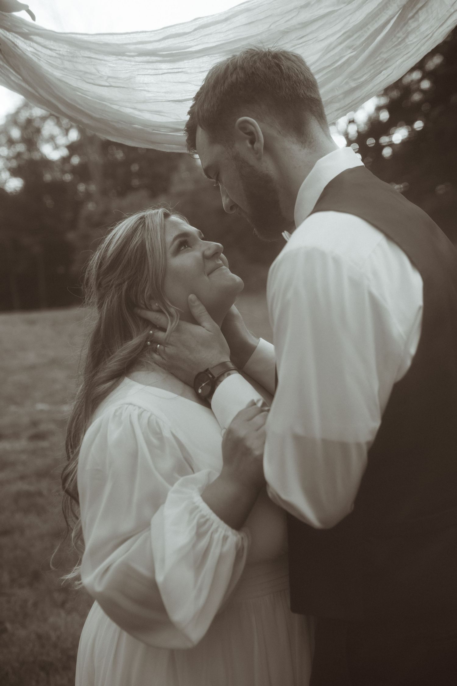 An intimate black and white wedding portrait with flowing white fabric in the background.