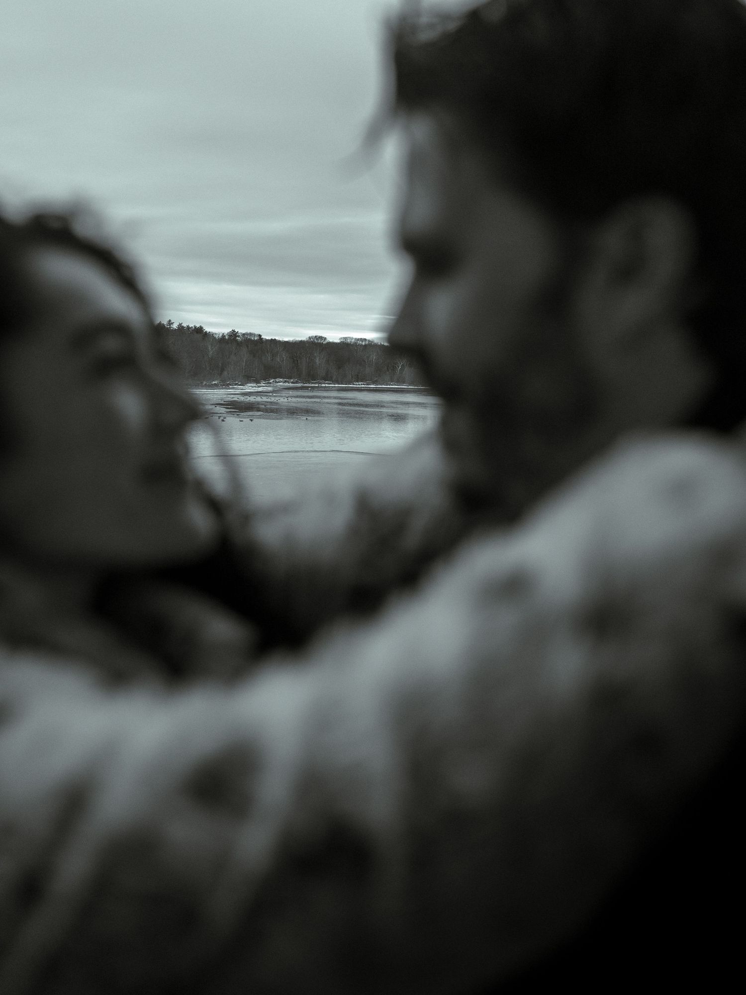 A series of blurred black and white photographs showing a couple in an intimate moment by a waterfront.