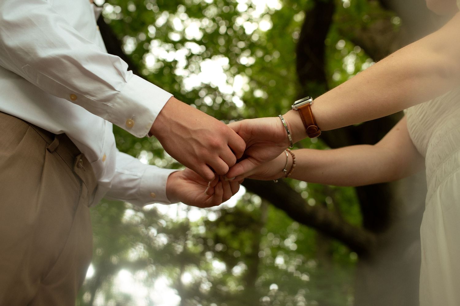 Close up of hands joining together in an intimate outdoor moment with soft bokeh background.