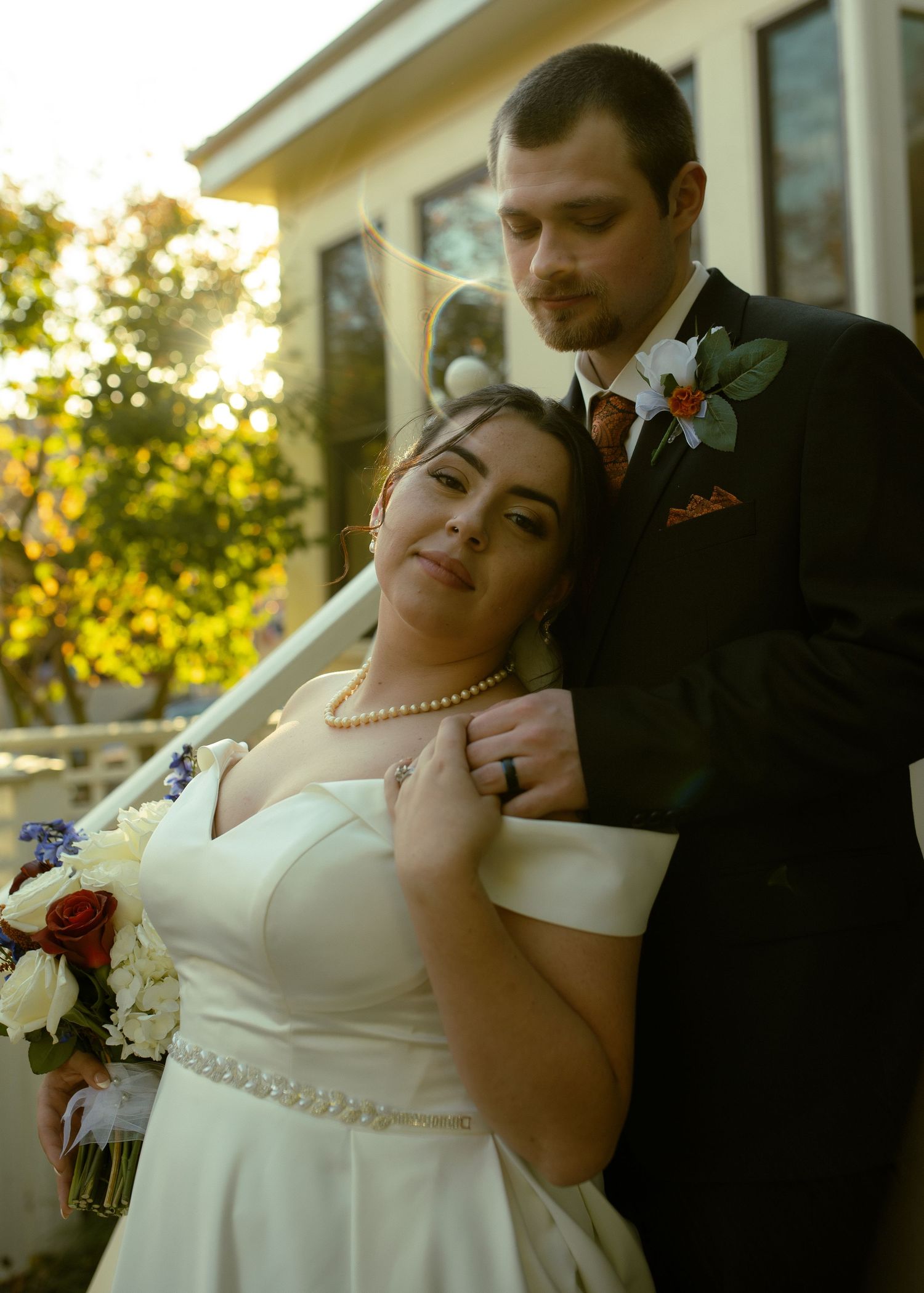 A bride and groom share a romantic moment during their wedding photoshoot at sunset with red roses in their bouquet.