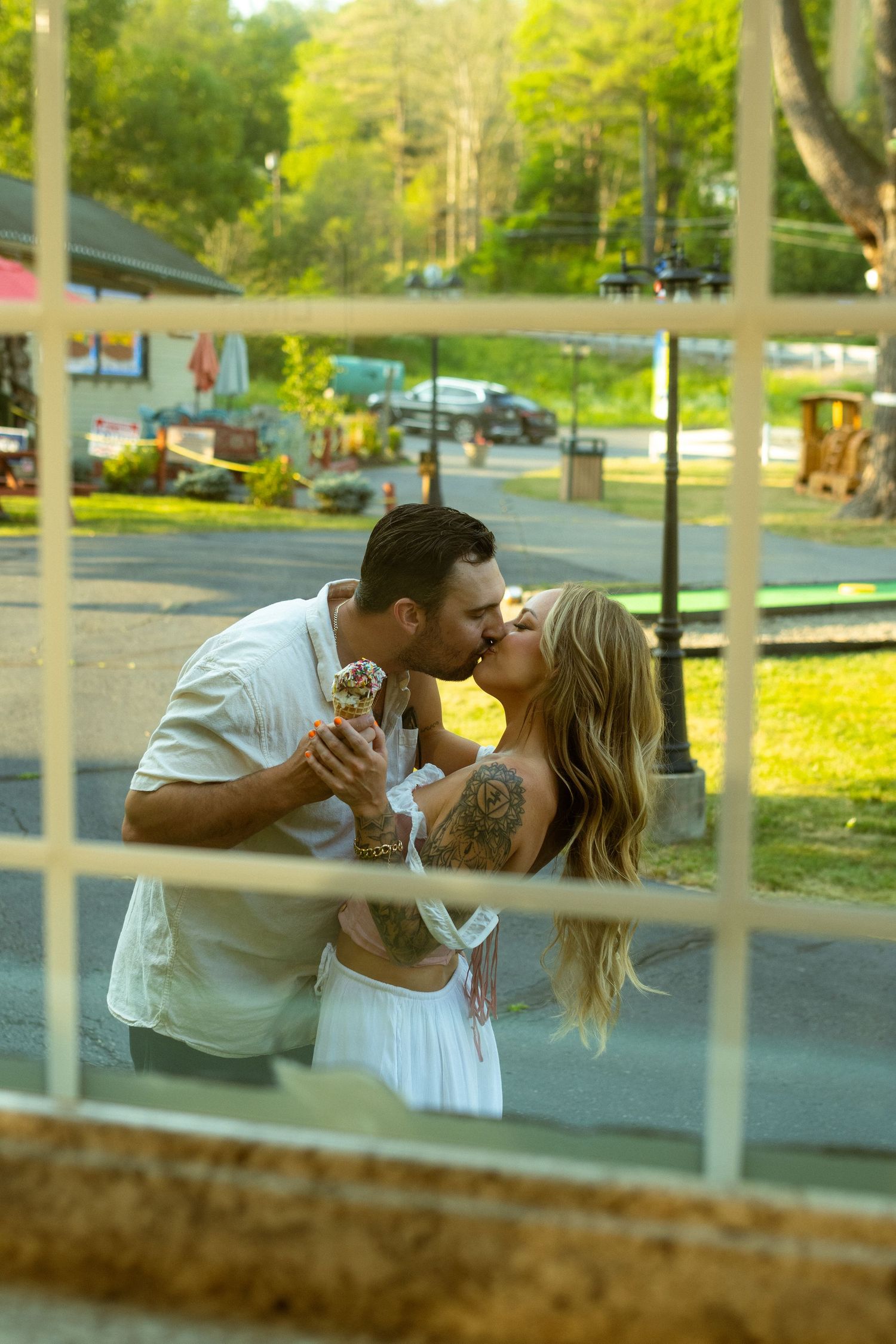 A couple sharing romantic moments through fence slats with sunlit yellow flowers in background.