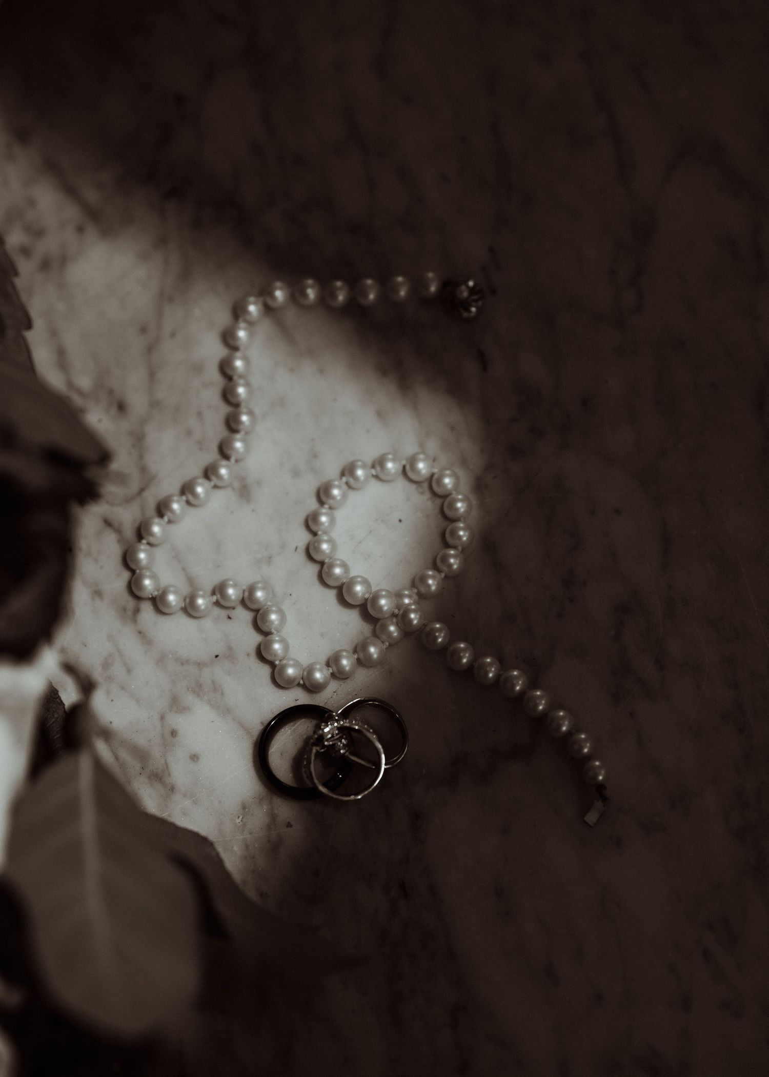 A series of black and white photographs showing pearl necklaces and rings arranged artistically on a textured surface.