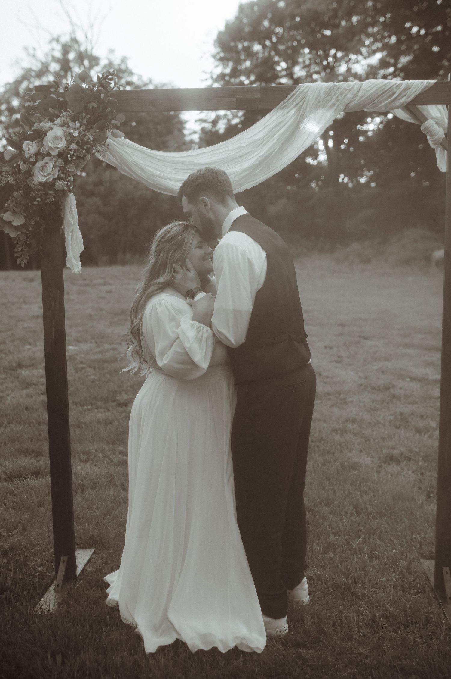 A romantic black and white wedding moment captured under flowing fabric outdoors.