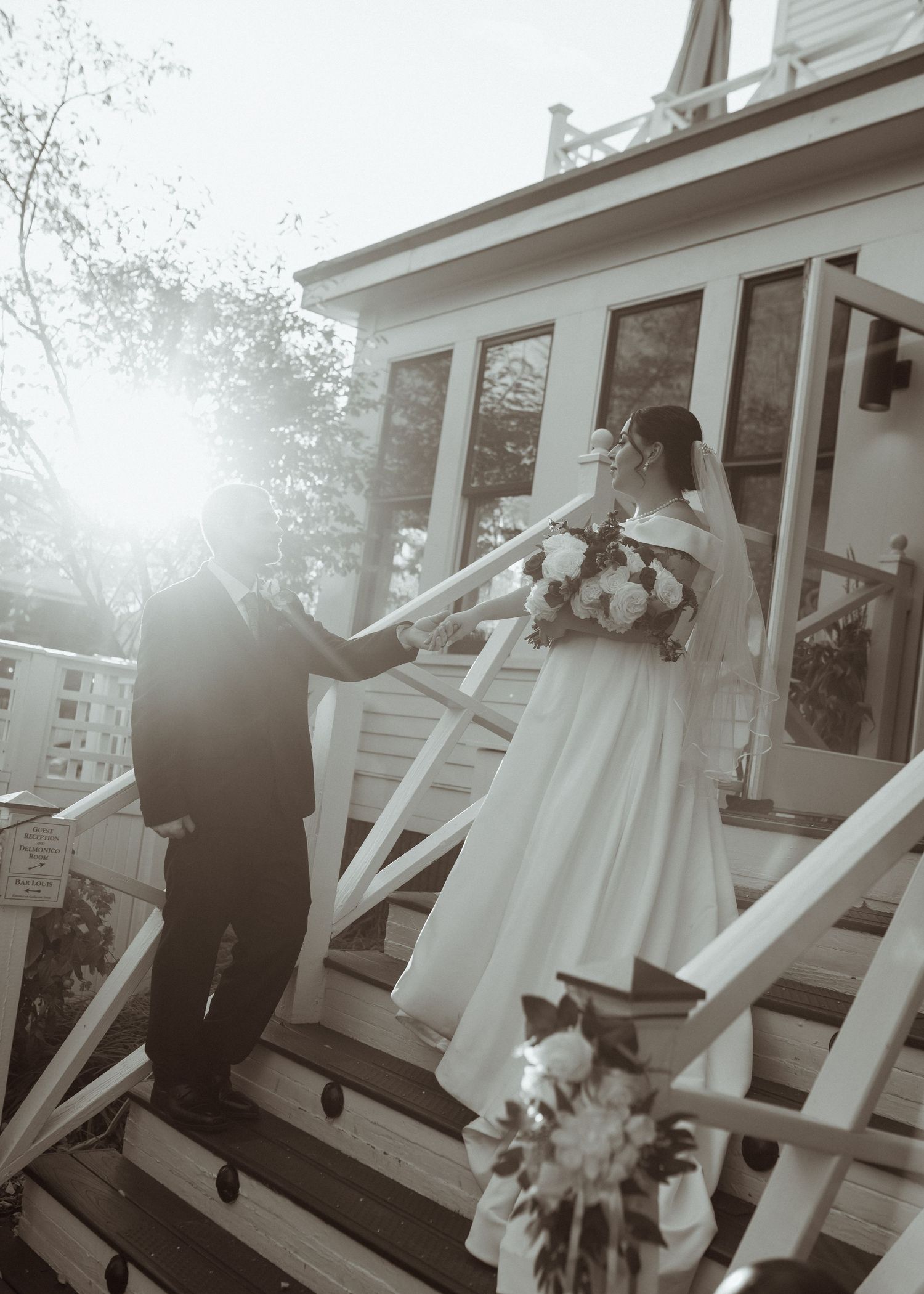A romantic wedding moment captured in black and white as a couple stands on a white porch with decorative railings.