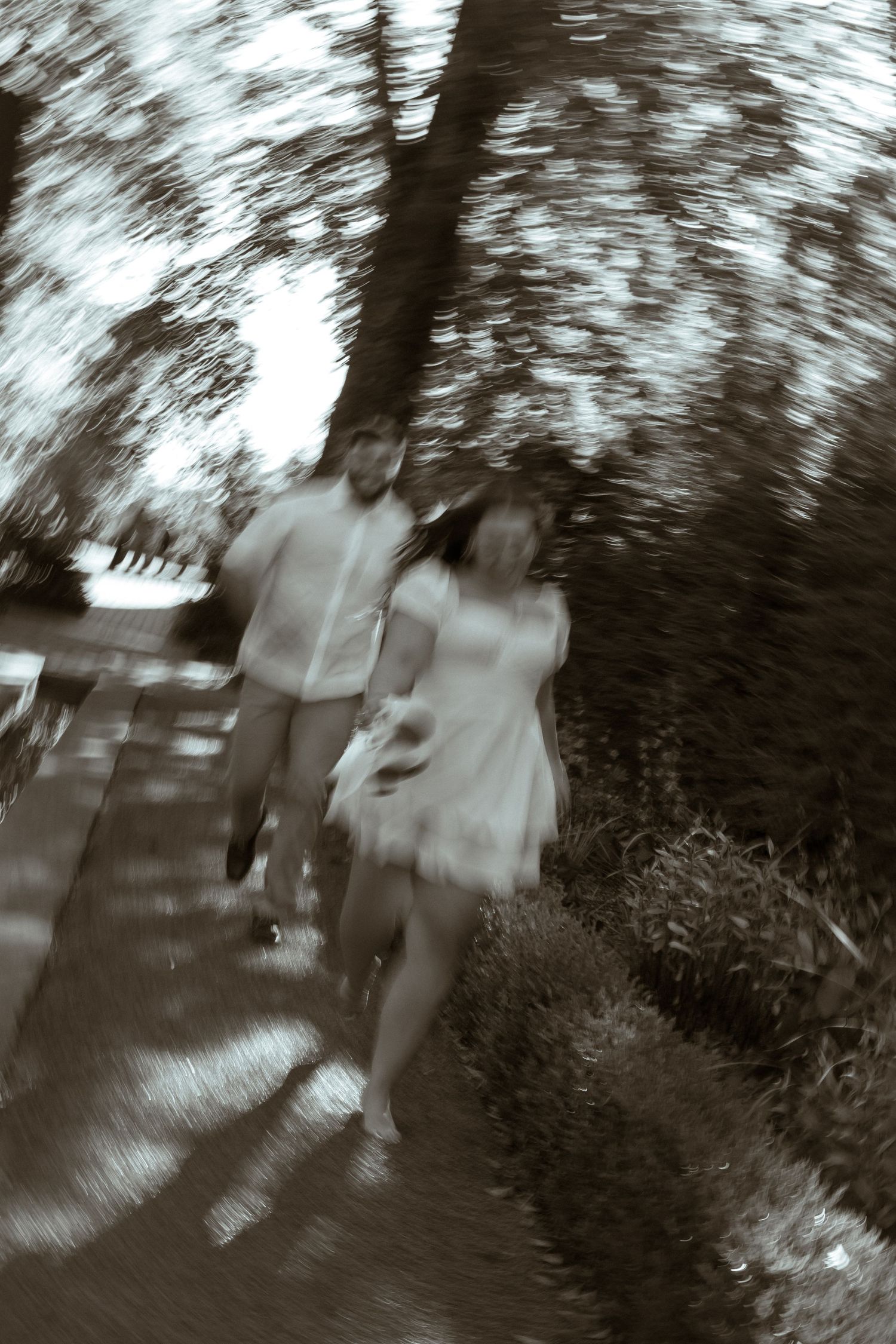 Motion-blurred black and white photograph showing figures walking through a wooded area.