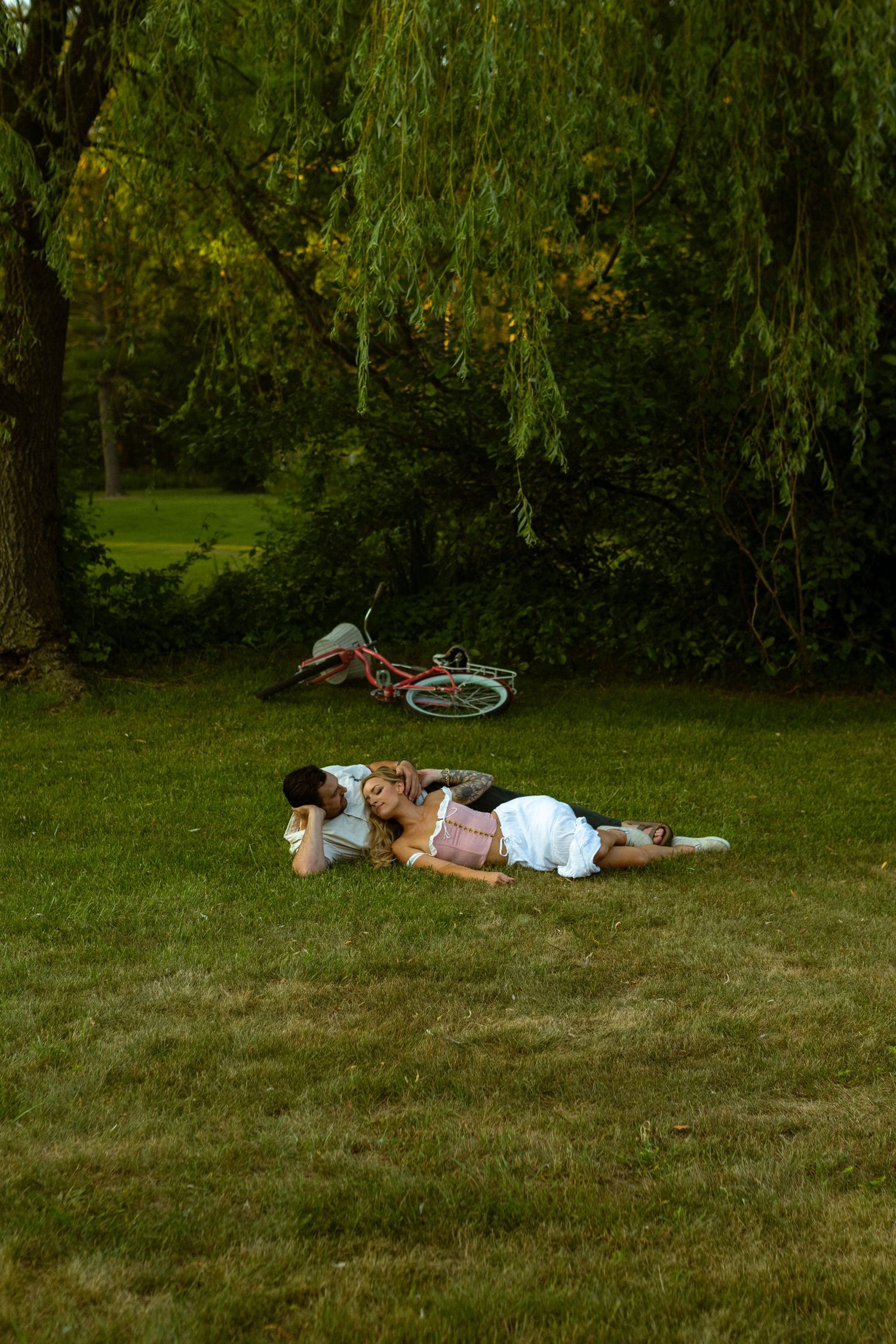 A romantic couple resting on grass with a bicycle visible in the background during golden hour.