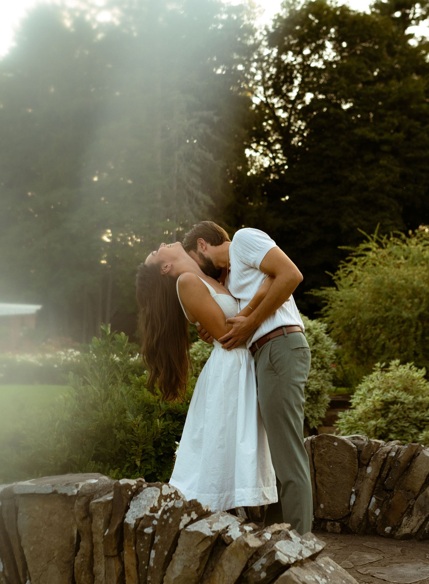 Intimate embrace captured during sunset on a stone wall in a garden setting.