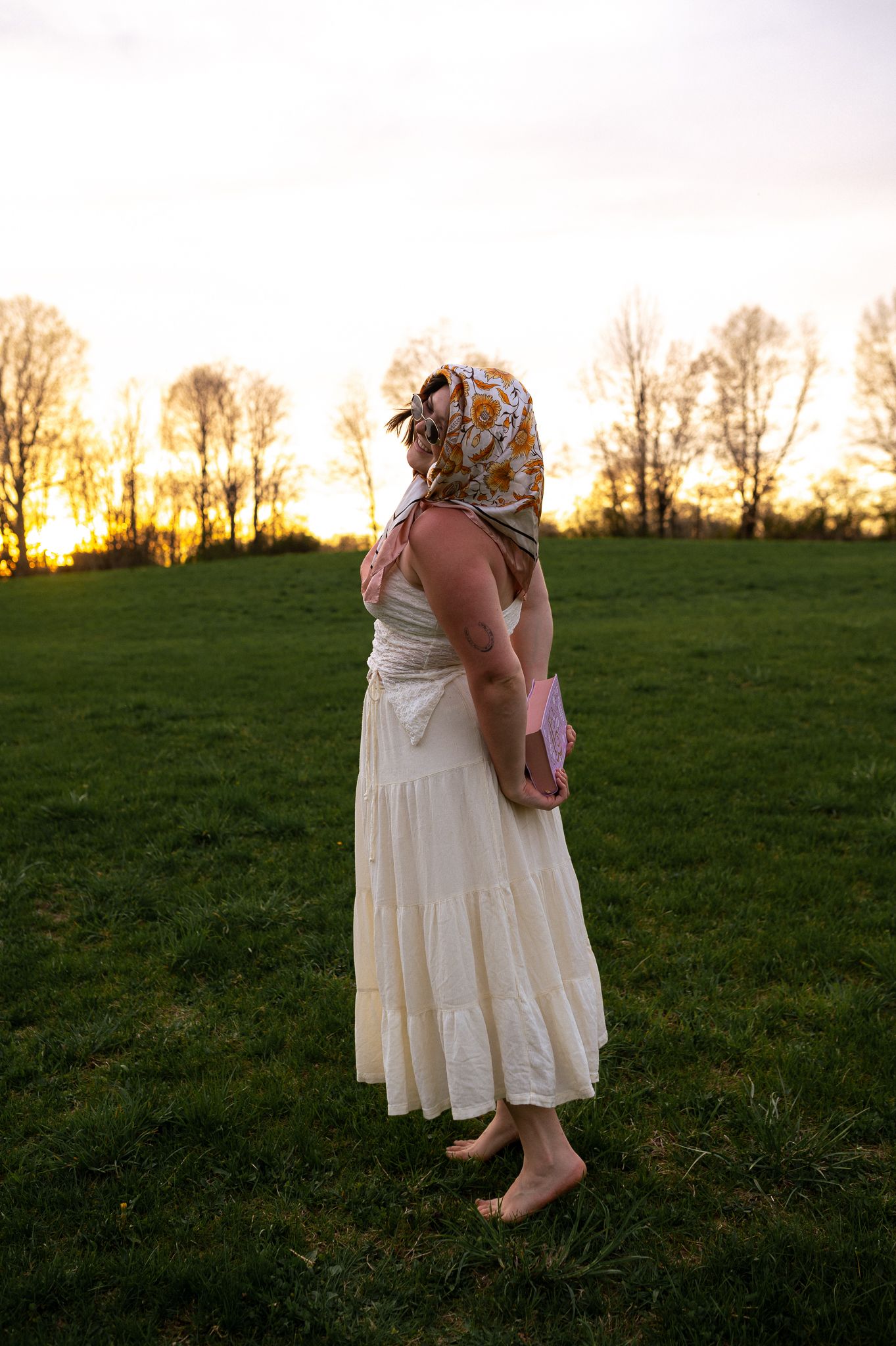 A couple in white dresses dance together in a grassy field at sunset.