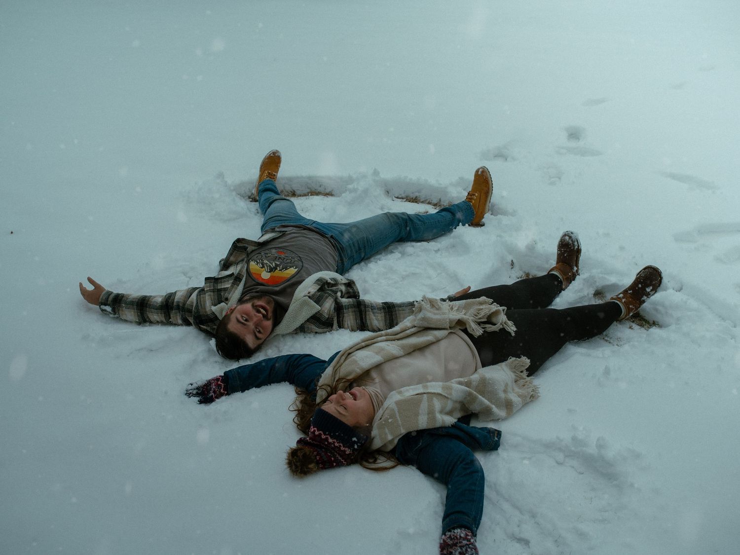 Three people lying in the snow making snow angels while wearing winter coats and boots.