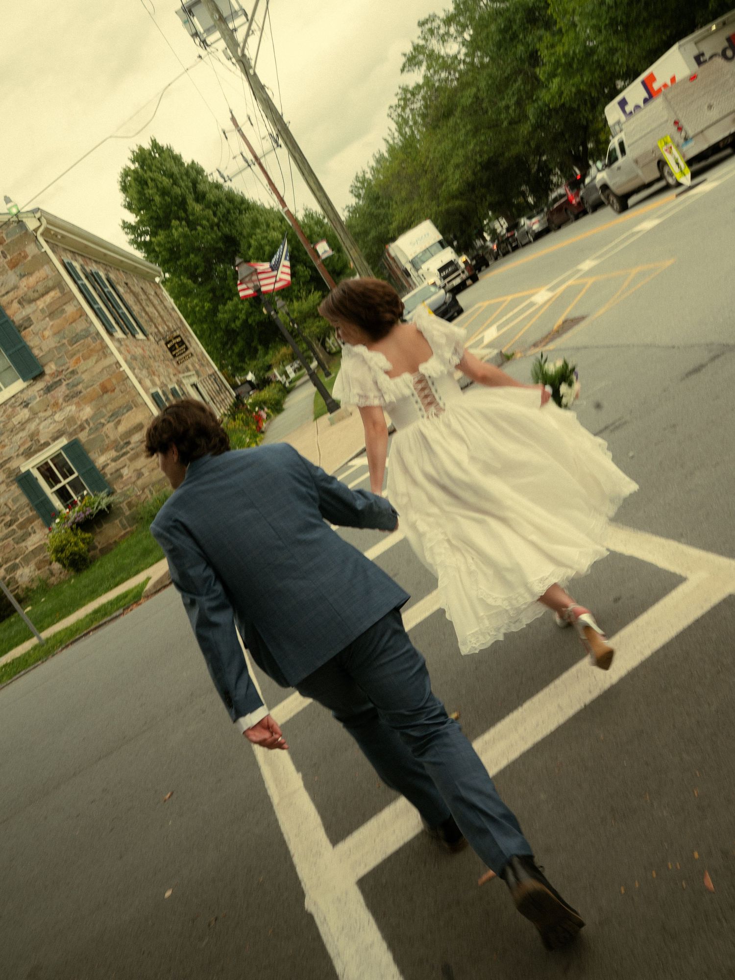 Bride and groom crossing a street hand in hand after their wedding ceremony on a cloudy day.