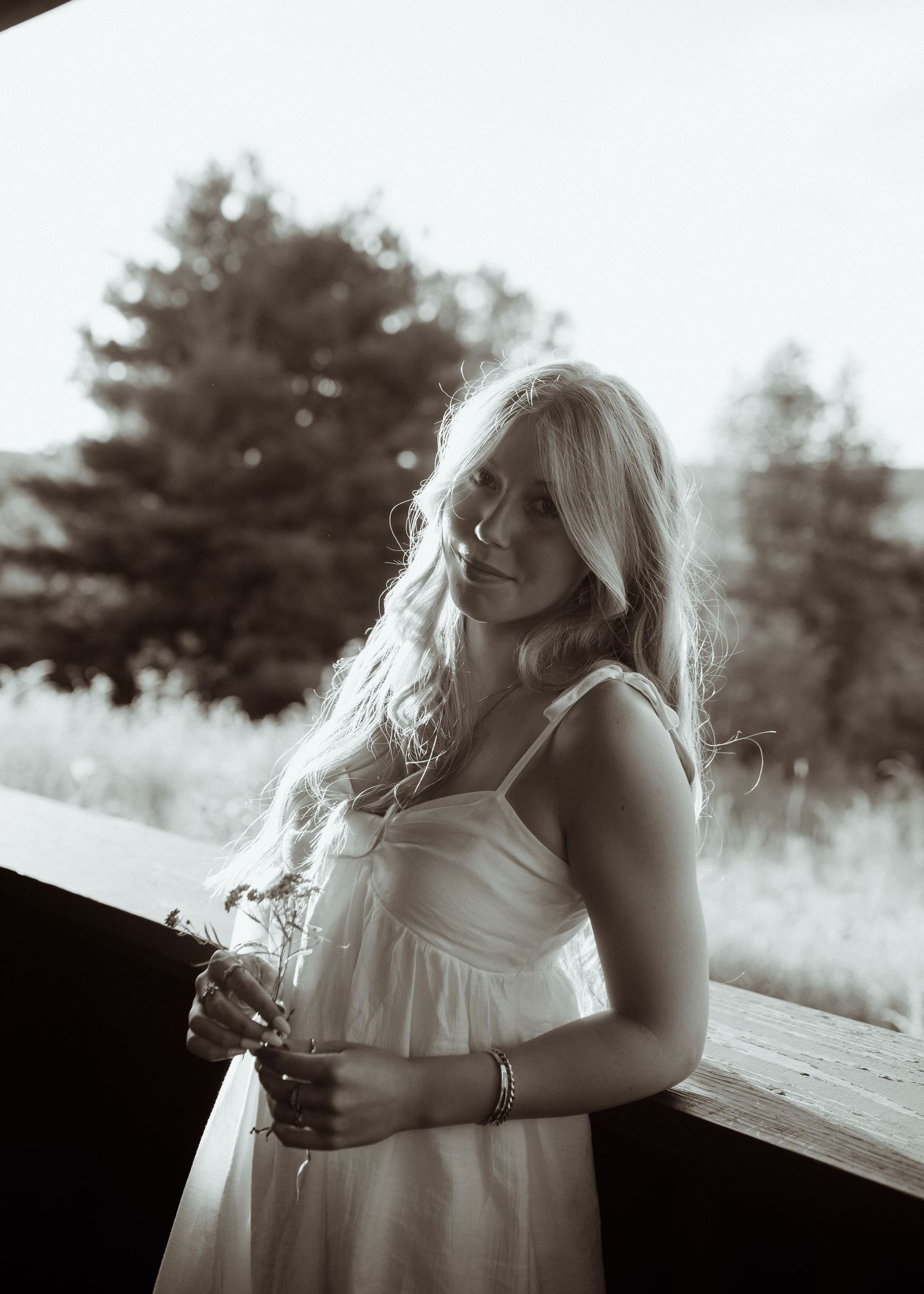 Artistic black and white portrait of someone in a white dress standing on a porch.
