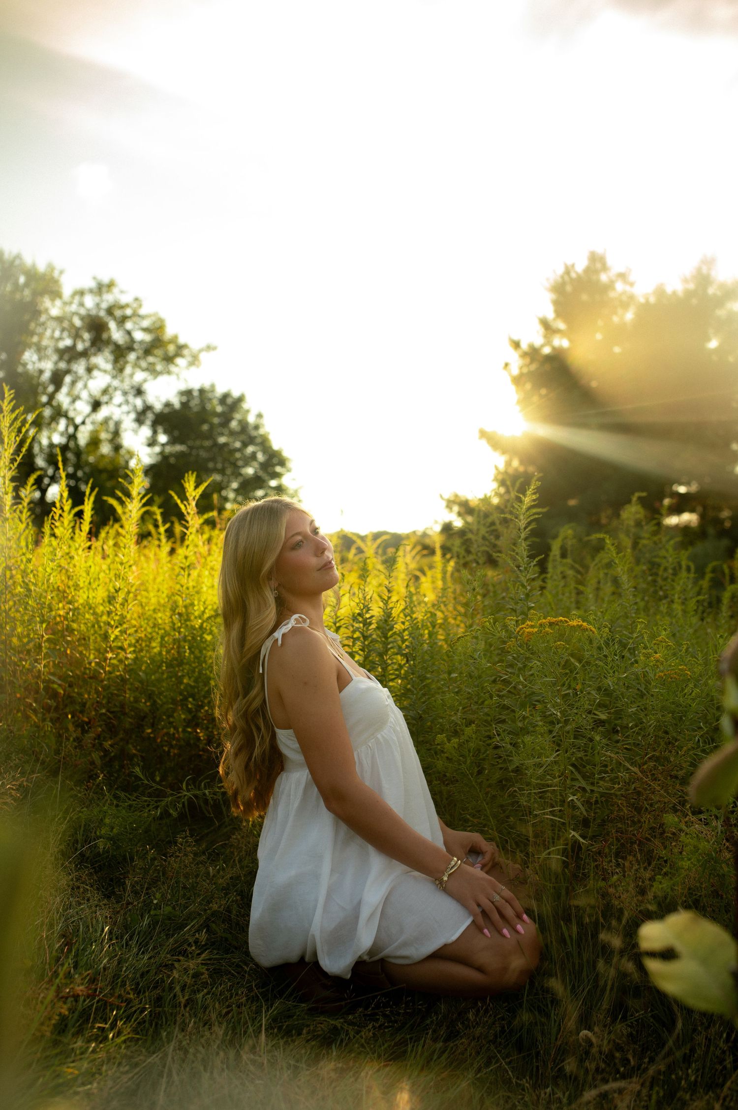 White-dressed figure sits peacefully among tall wildflowers at sunset.