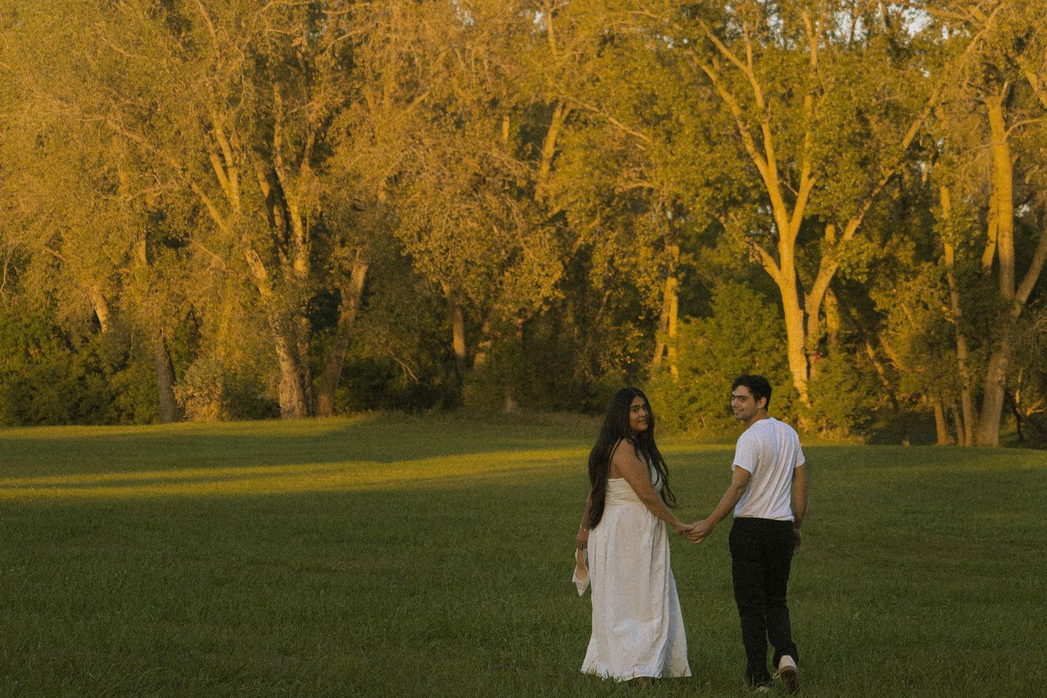 Couple holding hands looking back at sunset.