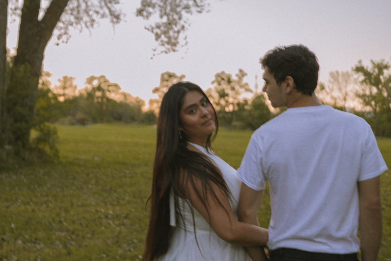 Girl holding partner's arm looking back at sunset.