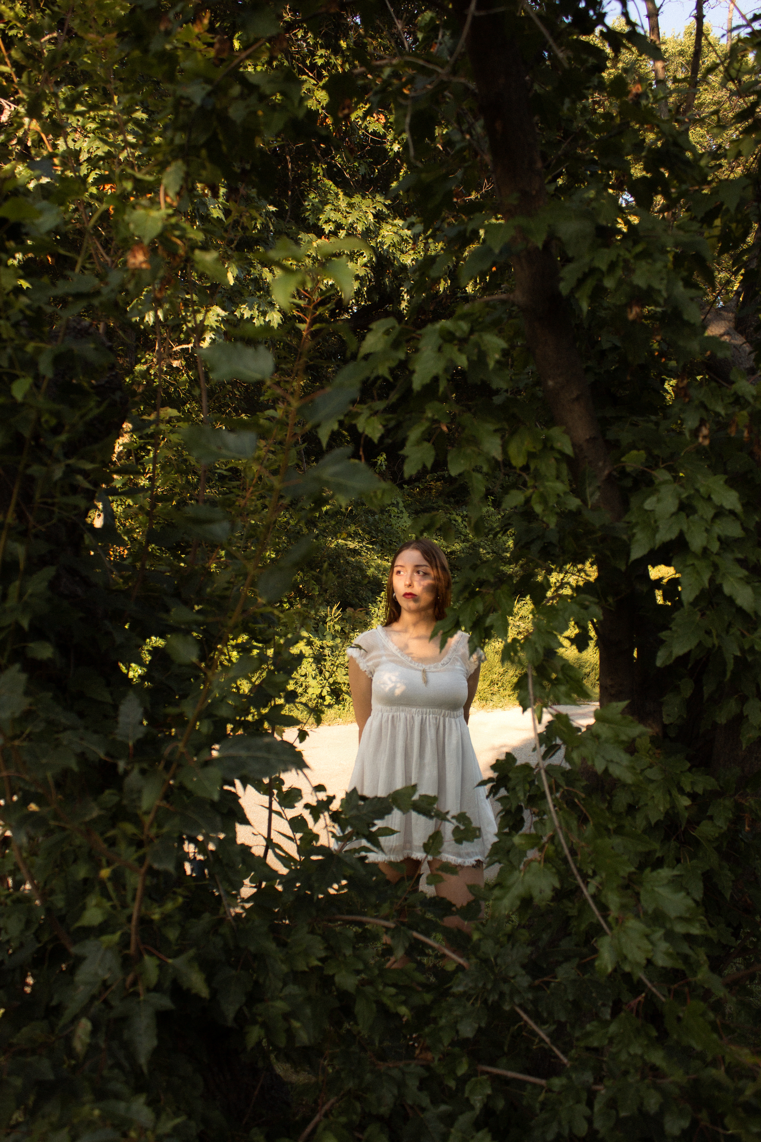 Girl behind trees sun-kissed by sunset.