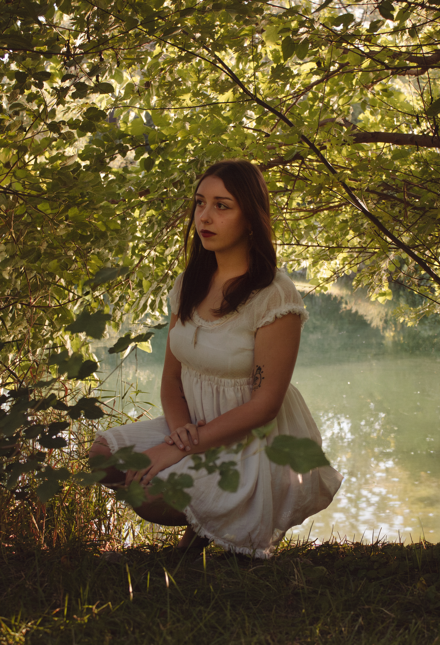 Girl kneeling in trees at lake.