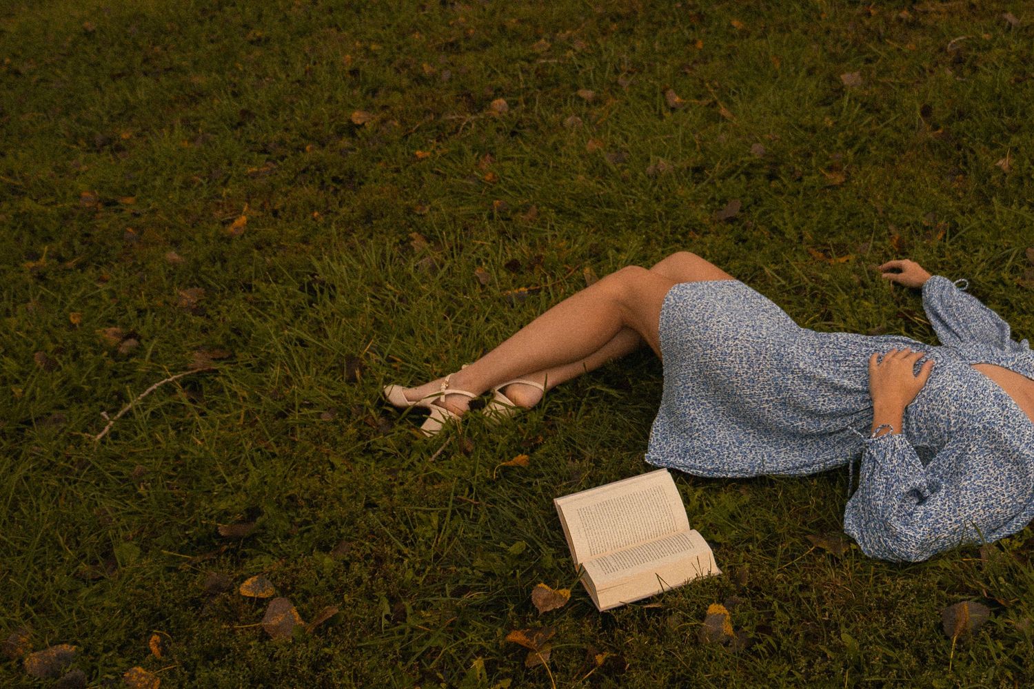 Girl laying in grass with book at dusk.