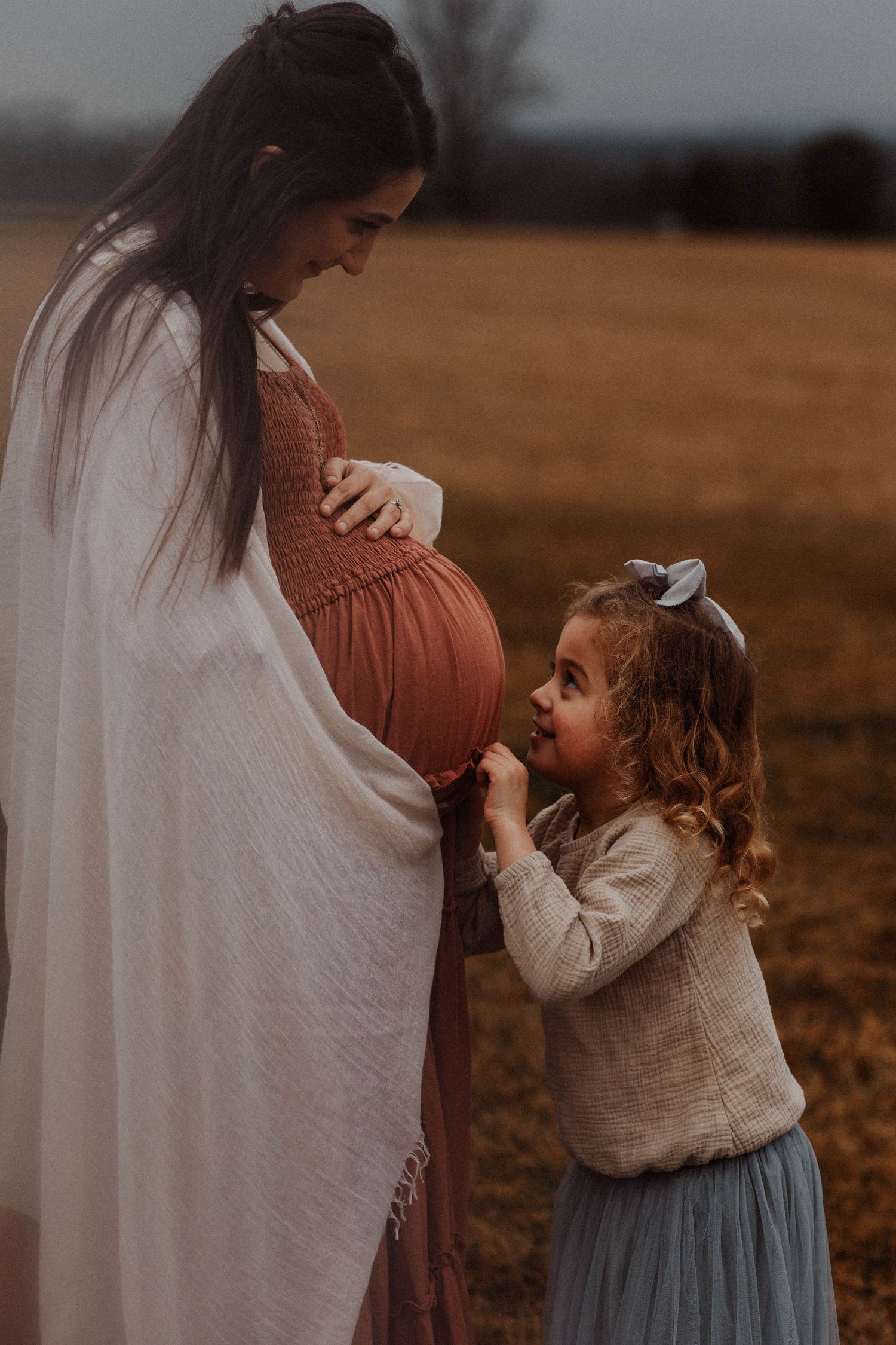 Sweet maternity moment captured in autumn field at sunset.