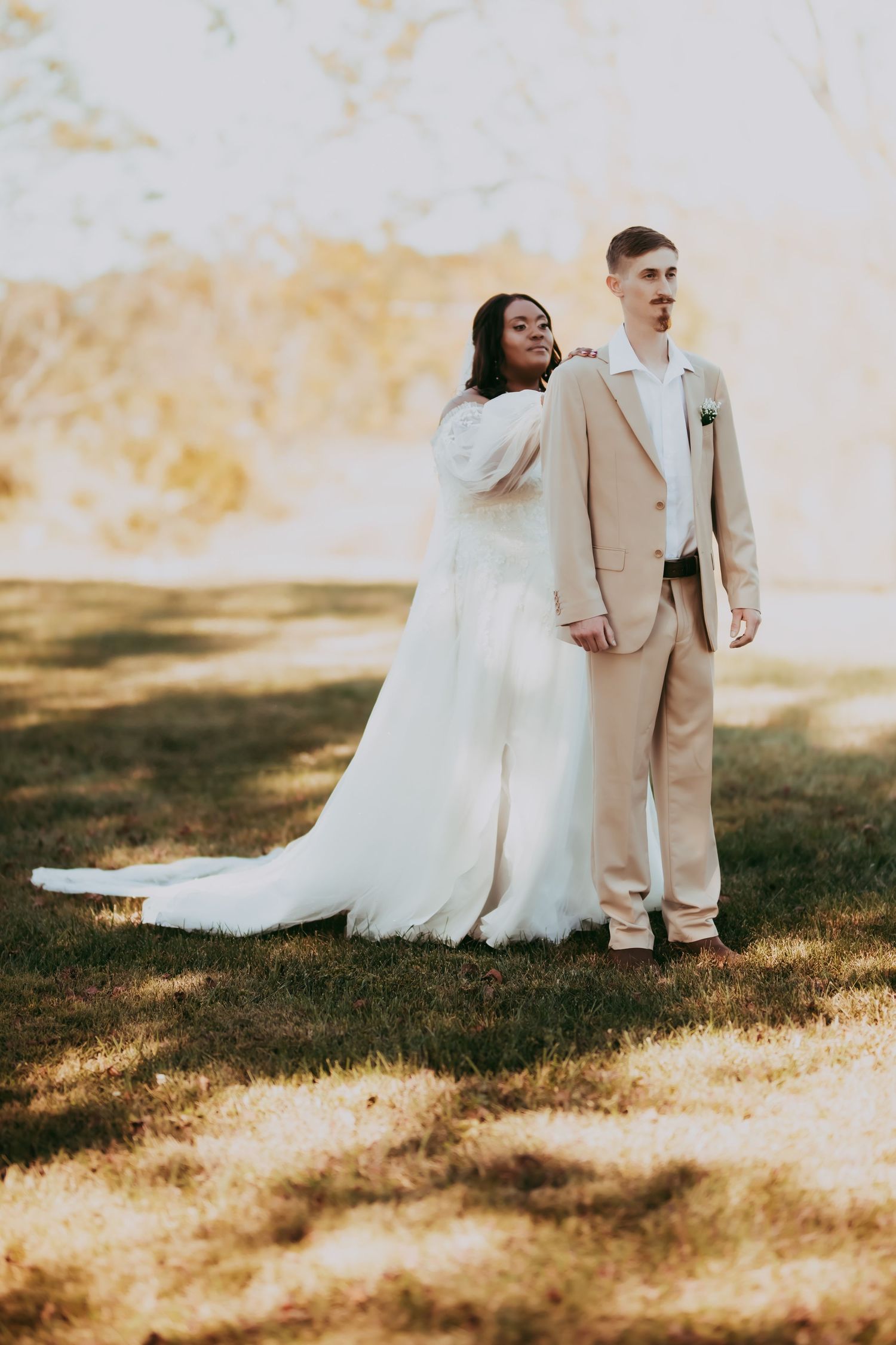 Wedding couple in elegant attire photographed in golden sunlight on grass.