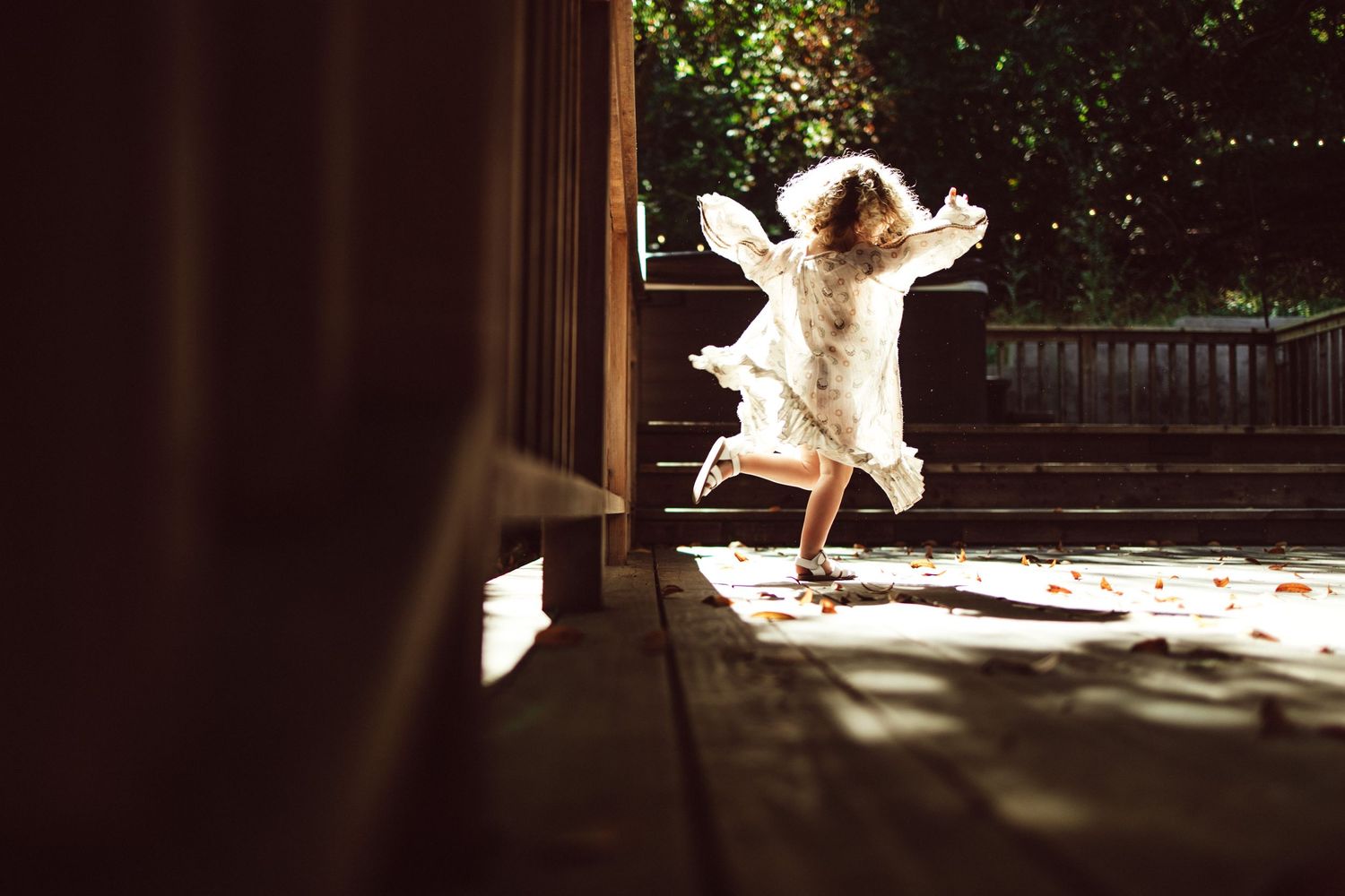 Silhouettes dancing and twirling on a sunlit wooden platform in a natural setting.