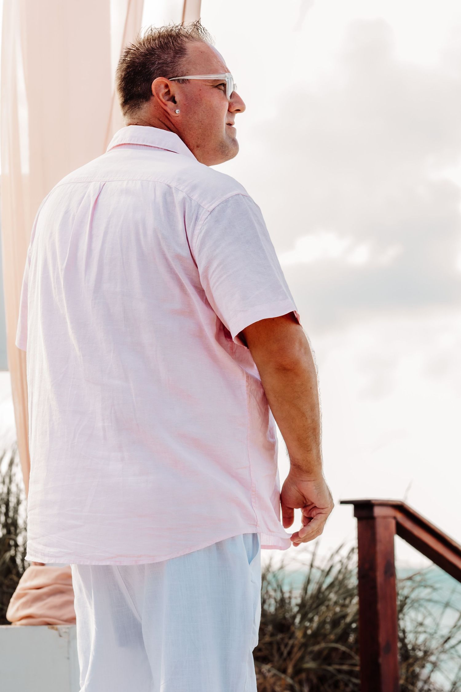 Groom awaiting his bride in a tropical destination alongside a beachside deck.
