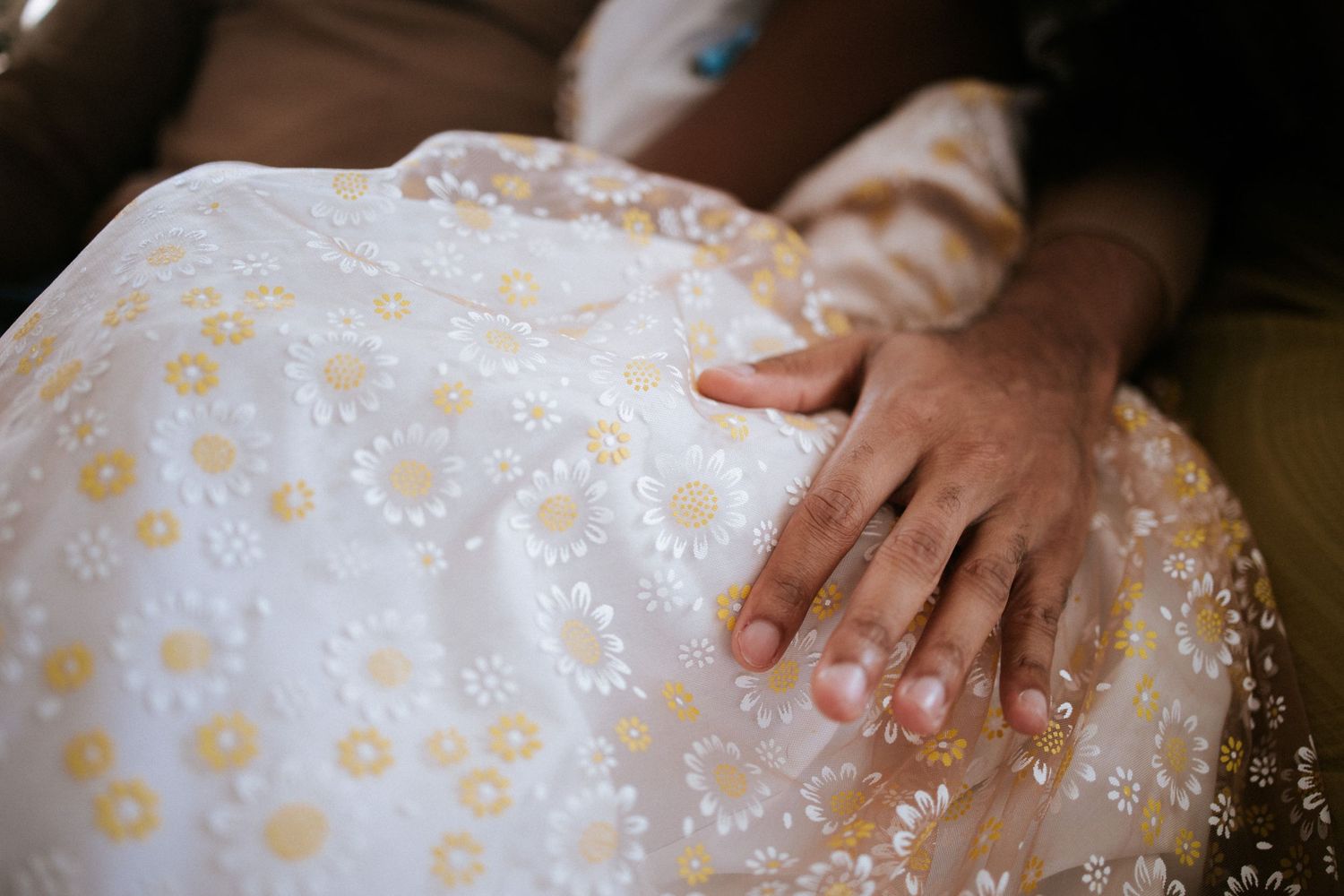 Delicate hands touch the fabric of a white dress with floral patterns.