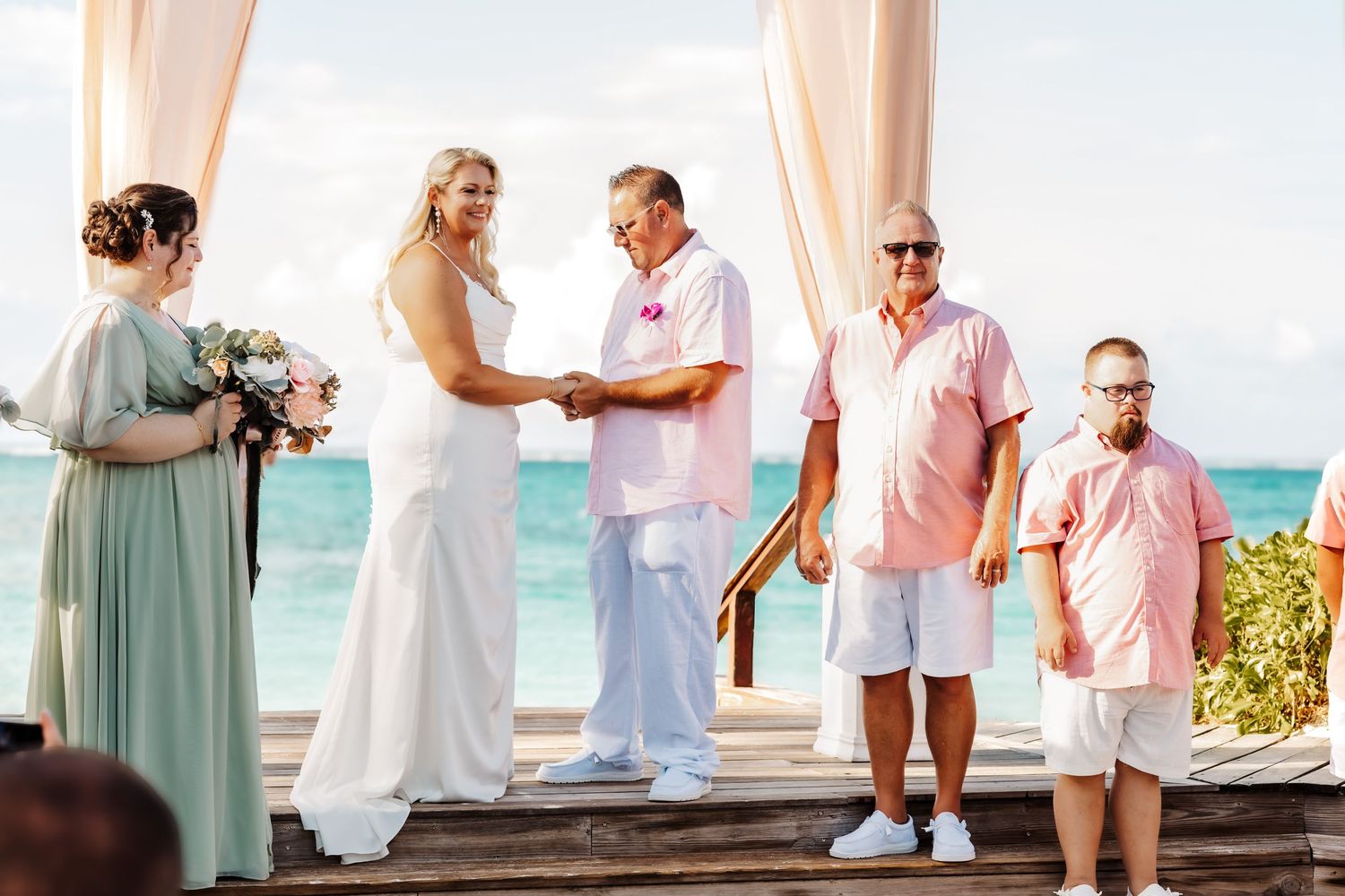 Wedding ceremony setup on a beach deck with white curtains and turquoise ocean views.