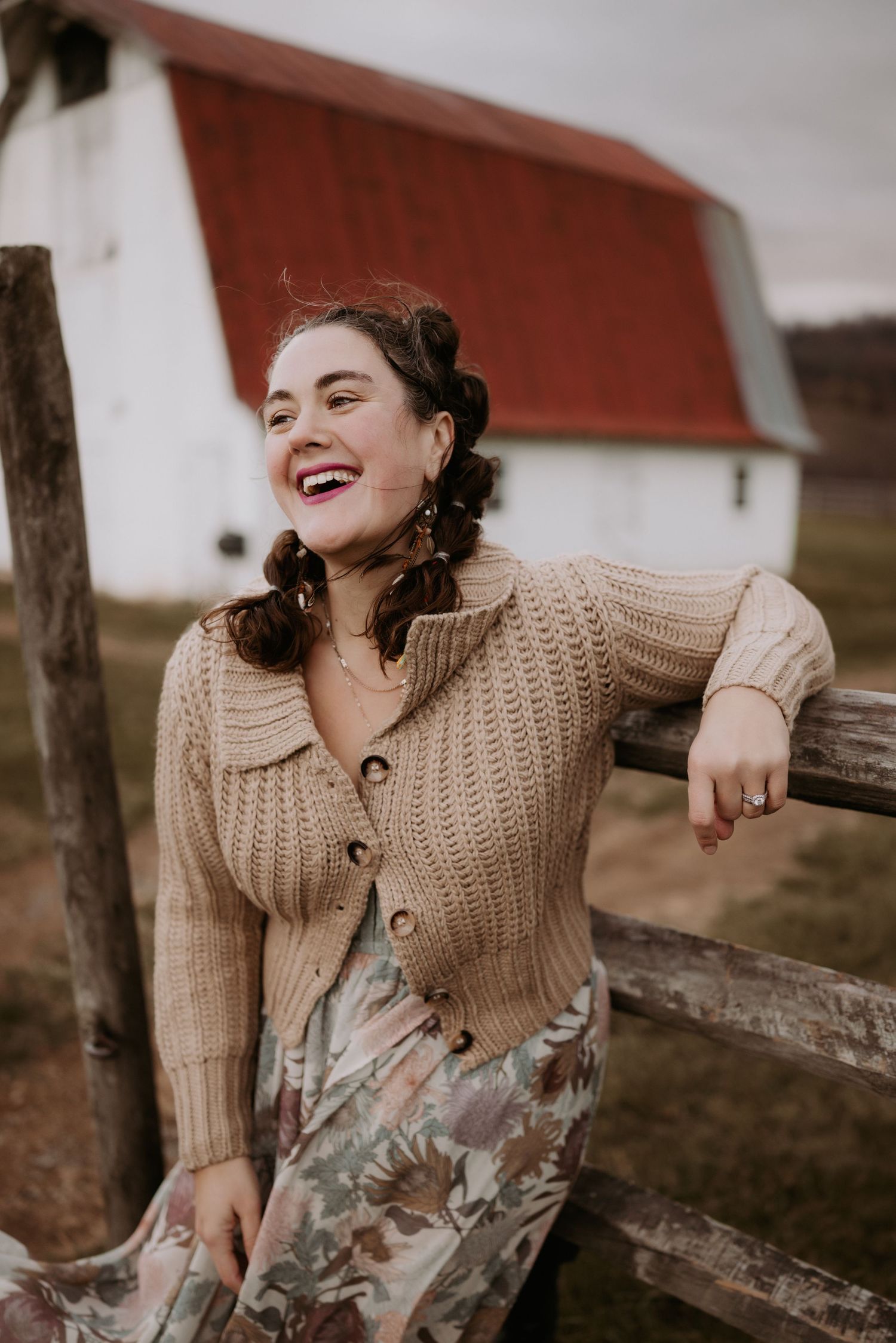 Woman in beige knit sweater laughs joyfully against rustic wooden backdrop.