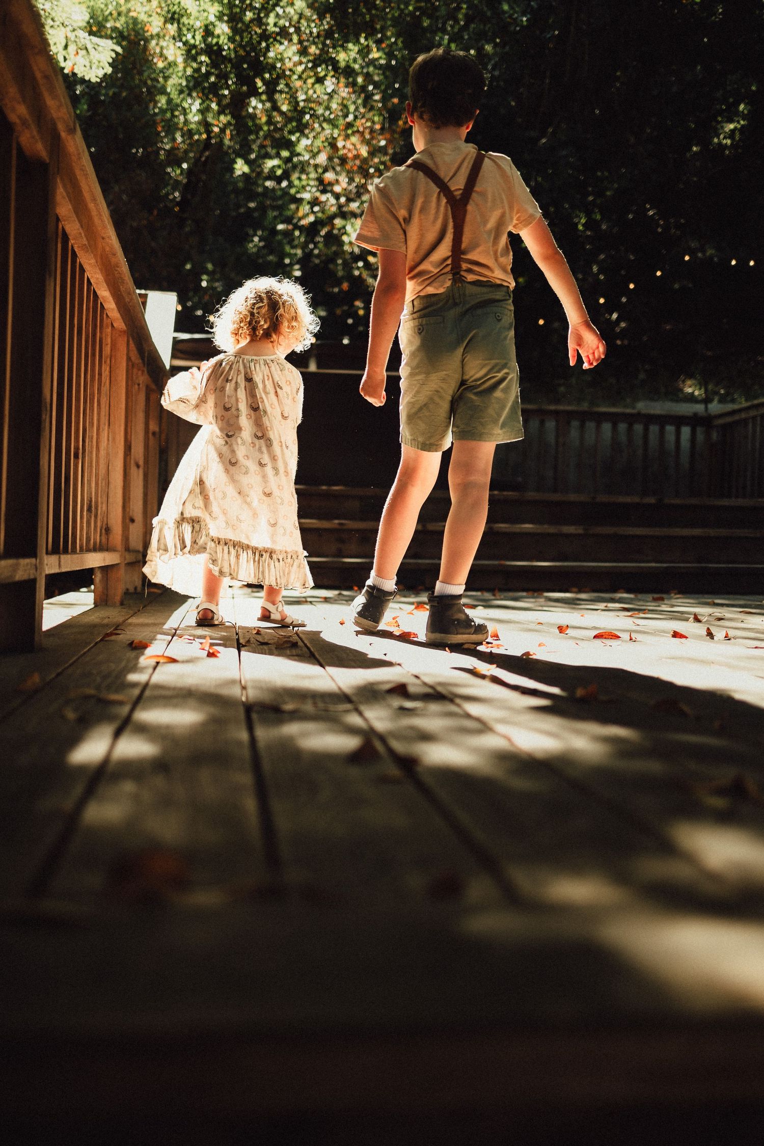 Low-angle shot of people walking on a sun-dappled wooden deck.