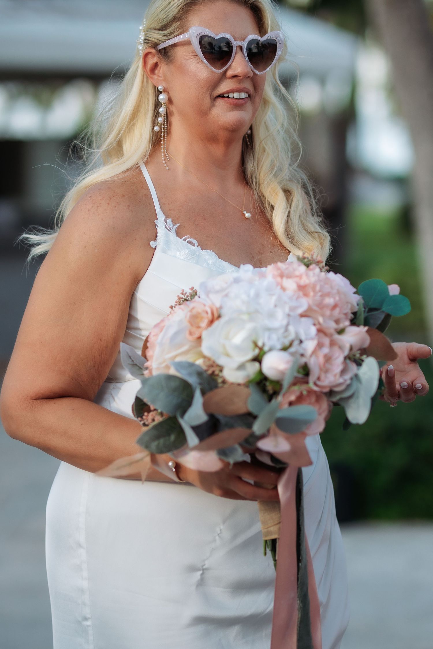 A wedding bouquet features soft pink and white roses with eucalyptus leaves in bride's hands.