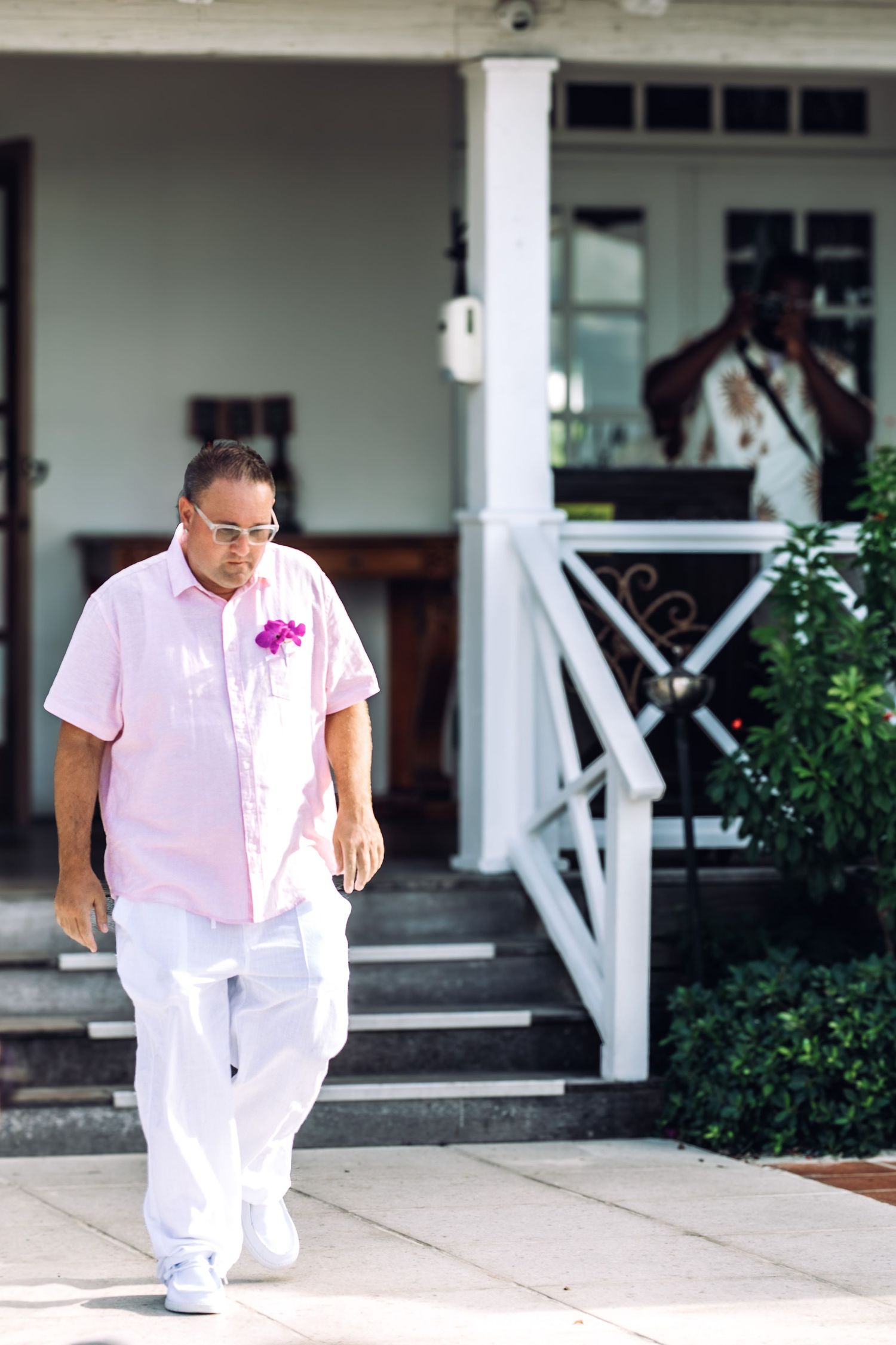 Groom walking along a covered porch with white columns at a destination wedding.