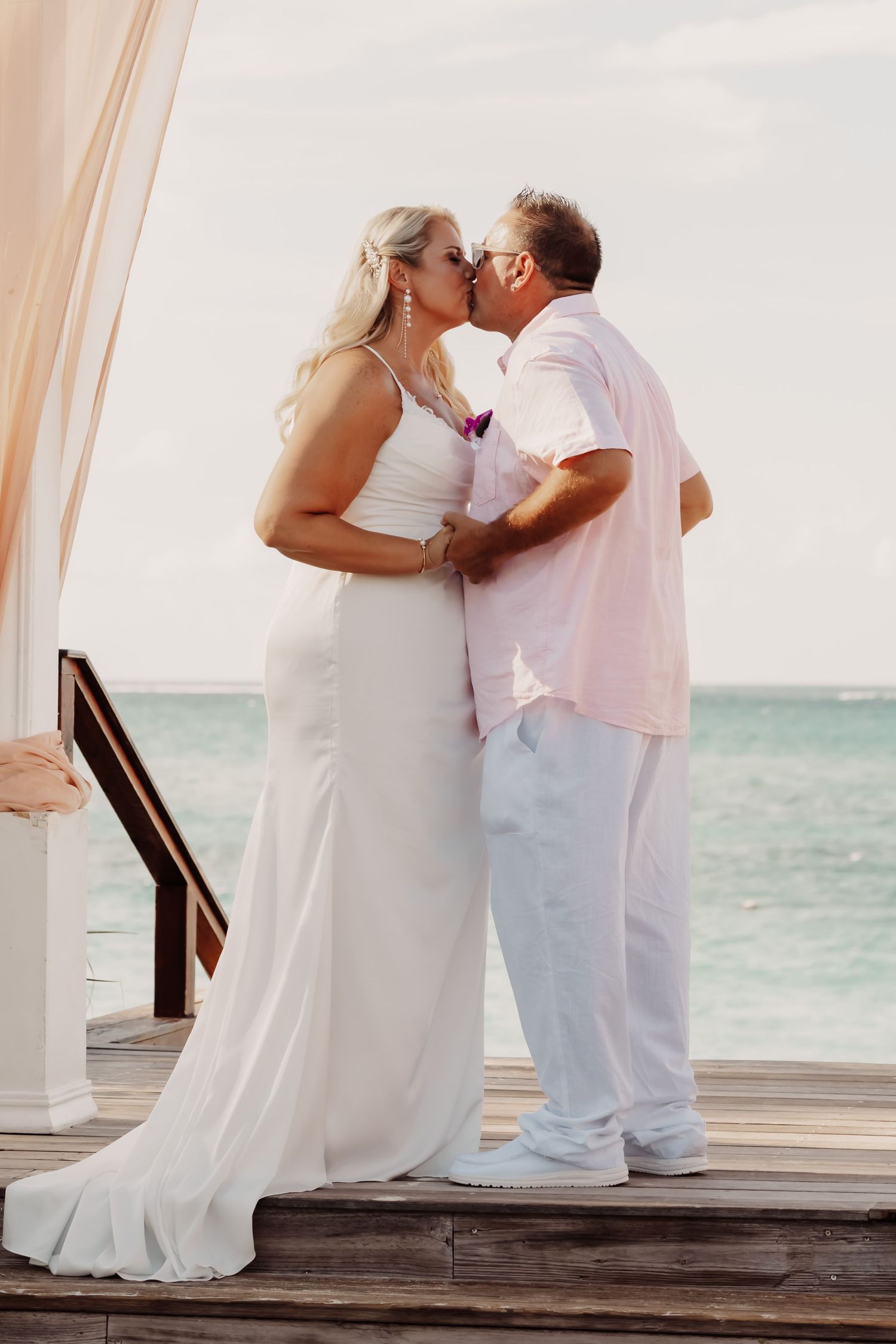 The bridge and groom sharing a romantic moment on a wooden deck overlooking the ocean.