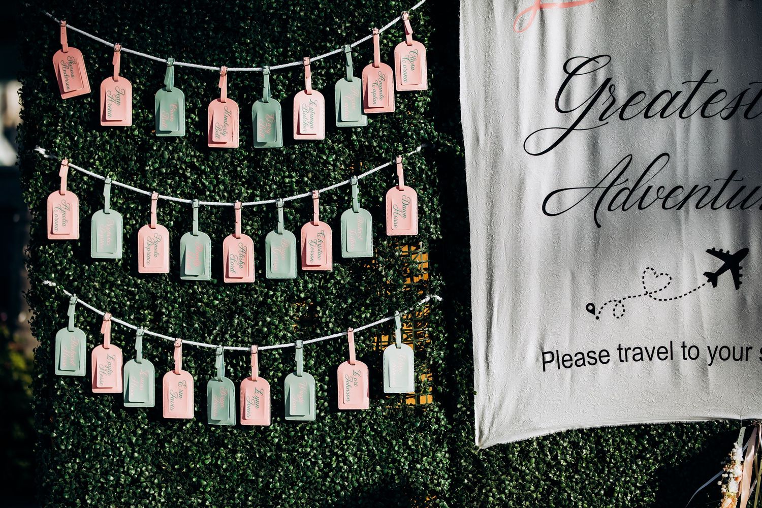 Pink and white hanging name tags create a decorative backdrop against a hedge wall to tell wedding guests where to sit.