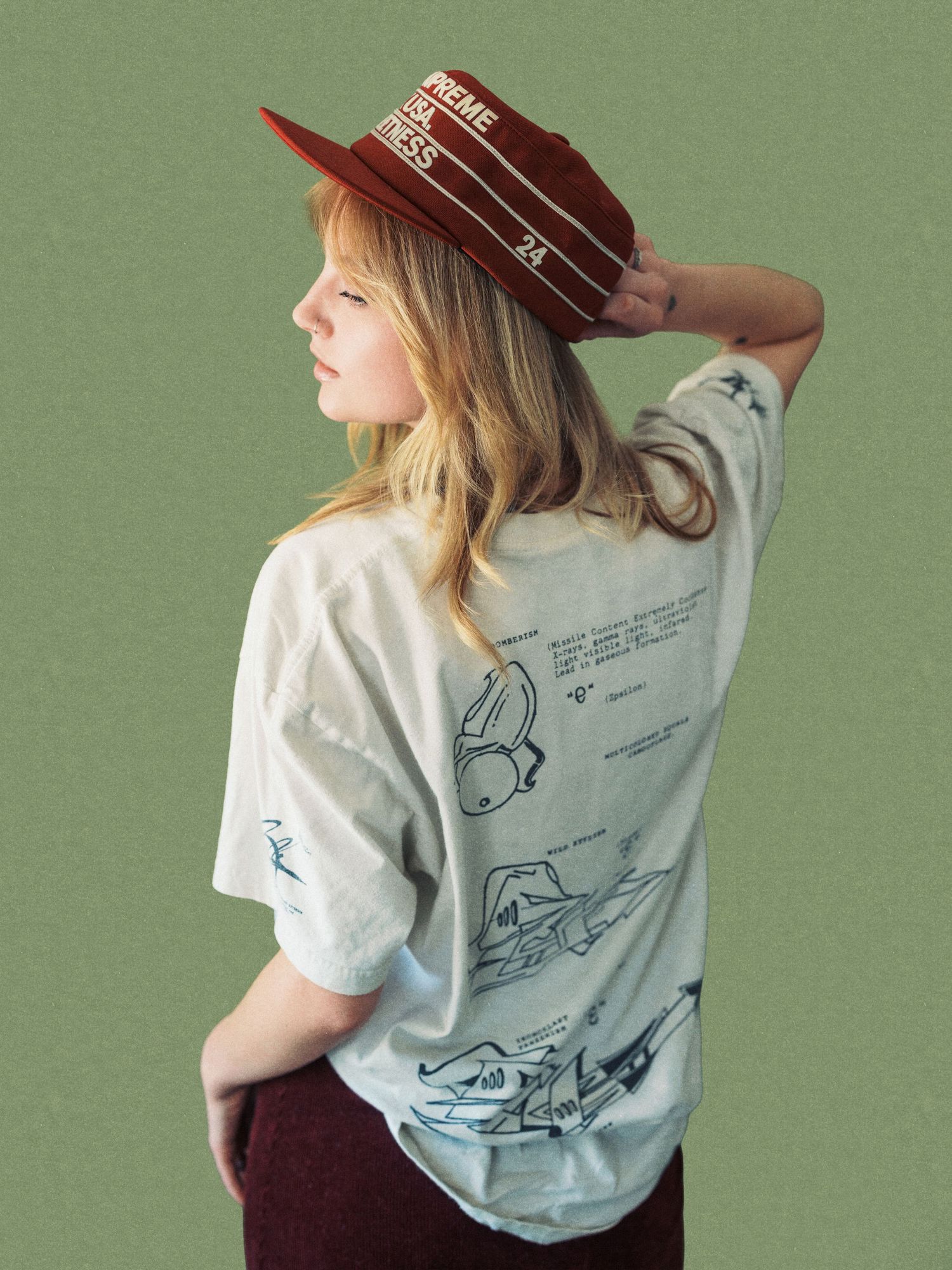 Woman wearing a graphic print oversized t-shirt and burgundy hat with Prime Fitness branding, posed against green background.