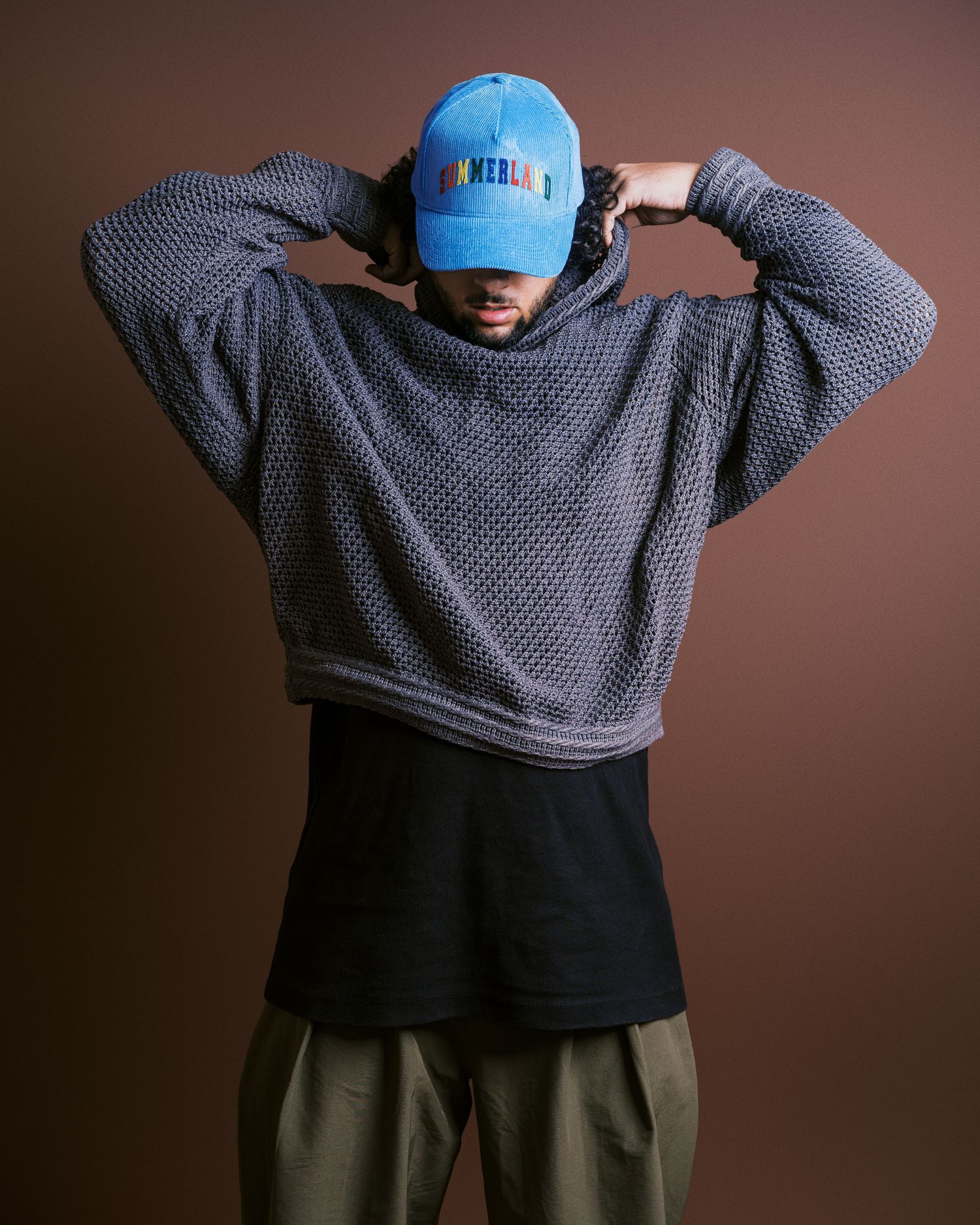 Person wearing a gray sweater and blue baseball cap shown from behind against a brown background.