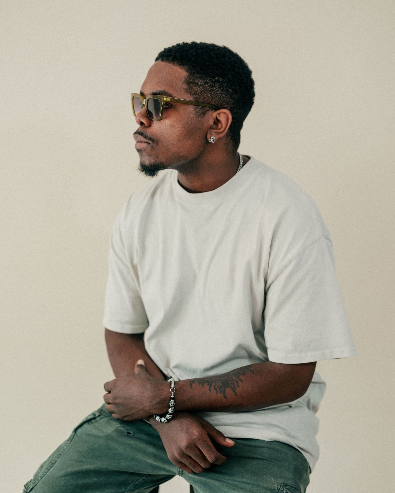 Figure in white t-shirt and casual wear sits thoughtfully against neutral backdrop.