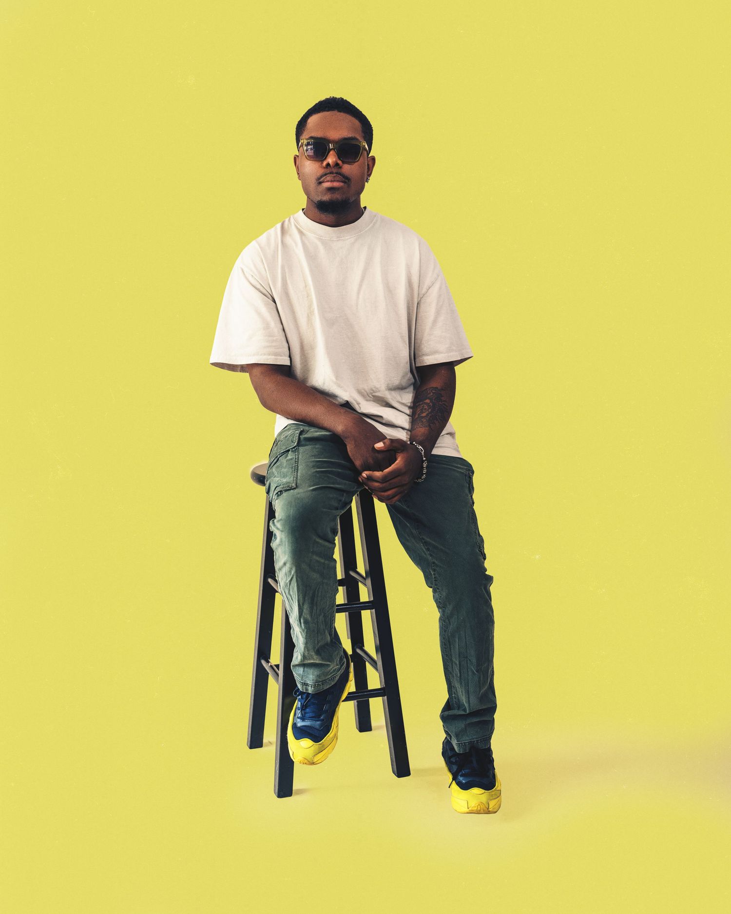 Person in white t-shirt and jeans sitting on black stool against yellow background in sequence of poses.