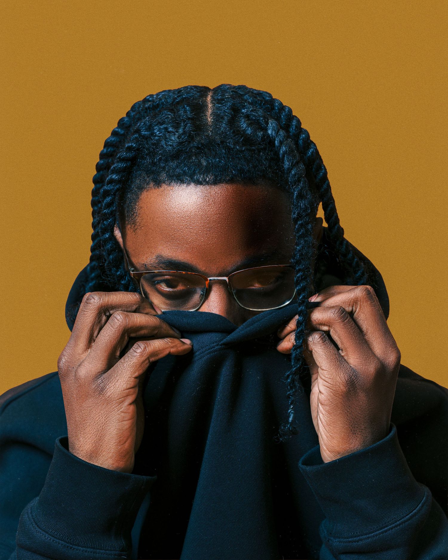 Sequence showing someone covering their eyes with a black turtleneck sweater against a golden brown background.